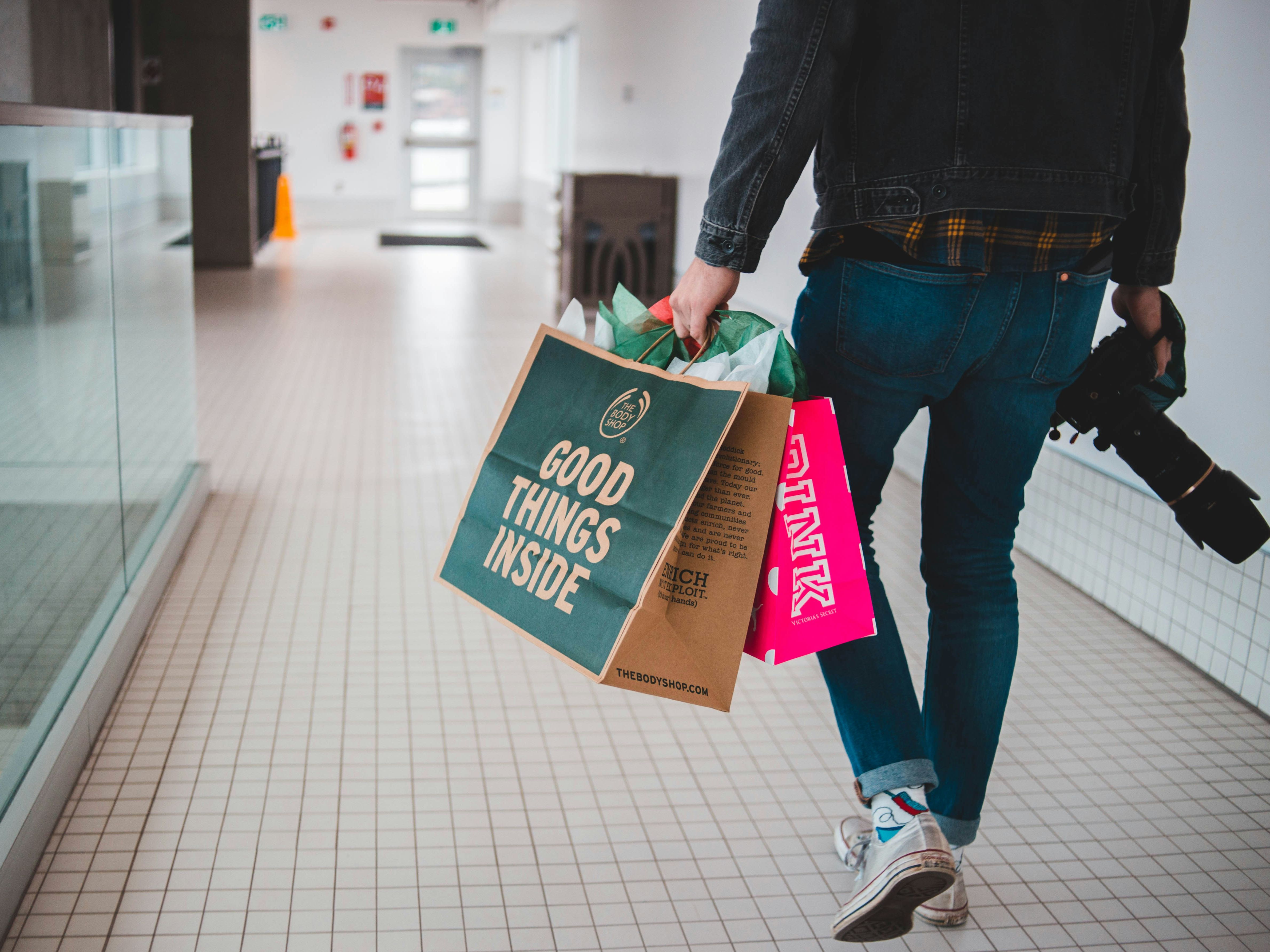 Person holding shopping bags and a camera walking in a hallway