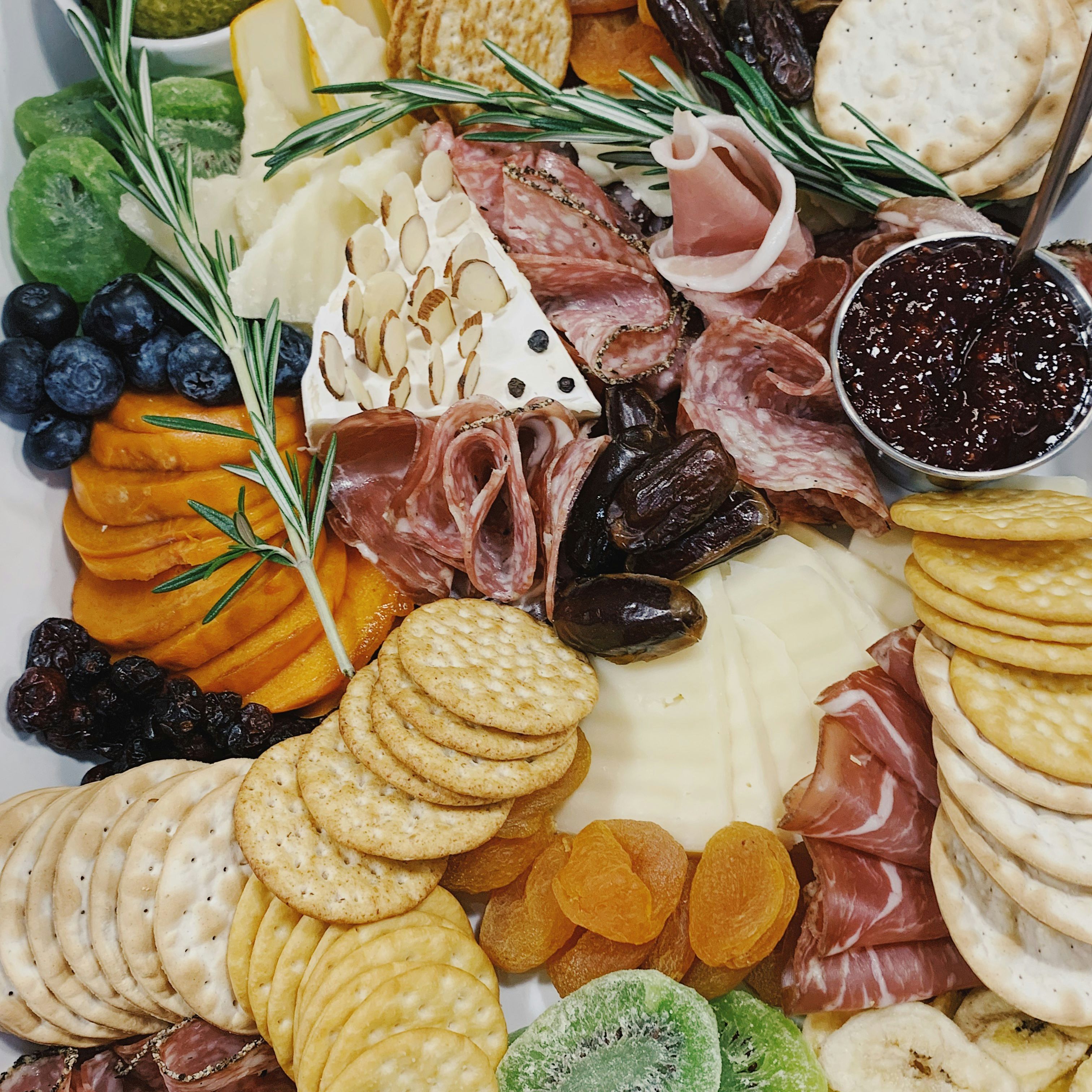 A charcuterie board with assorted crackers, cheeses, fruits, olives, nuts, and cured meats