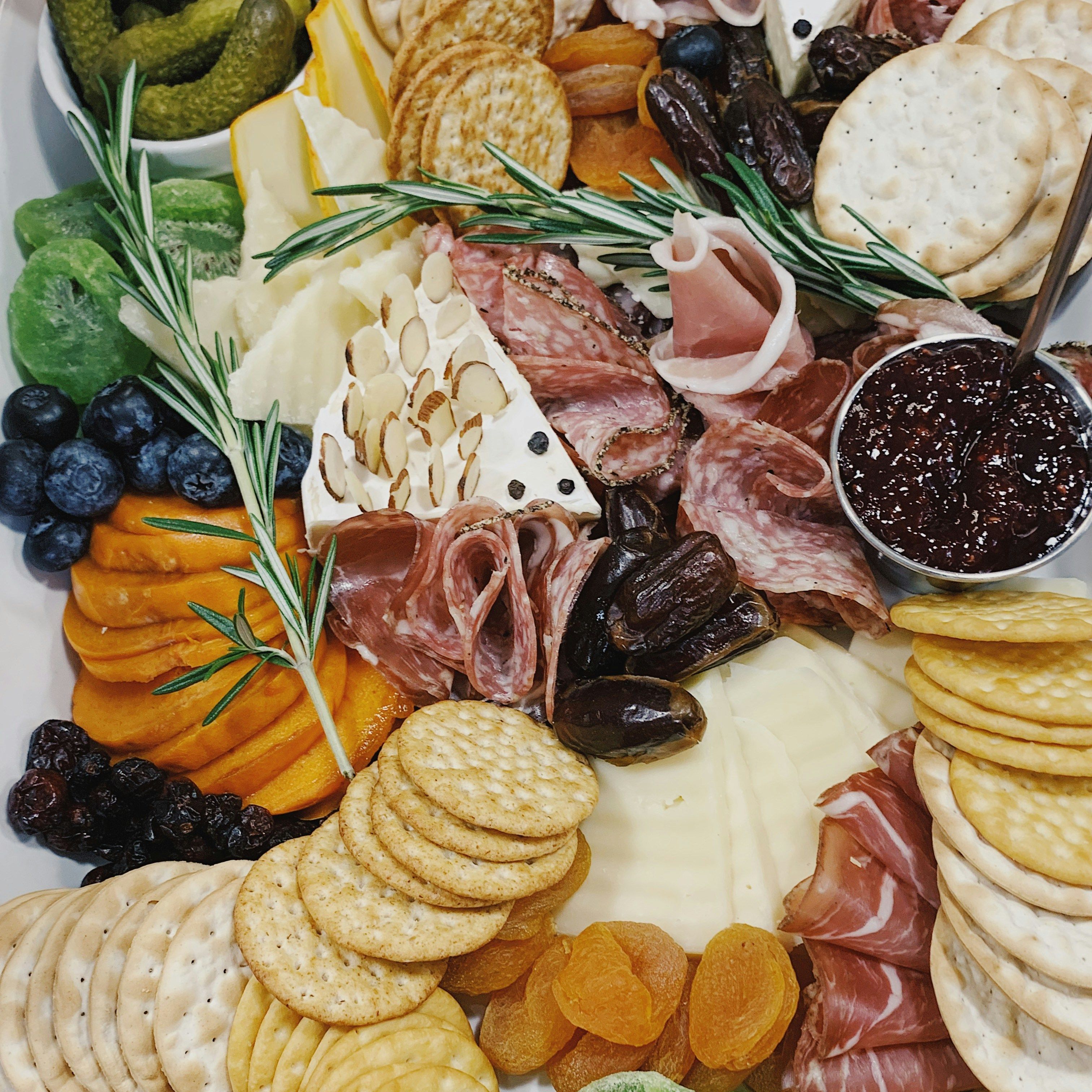 A charcuterie board with assorted crackers, cheeses, fruits, olives, nuts, and cured meats