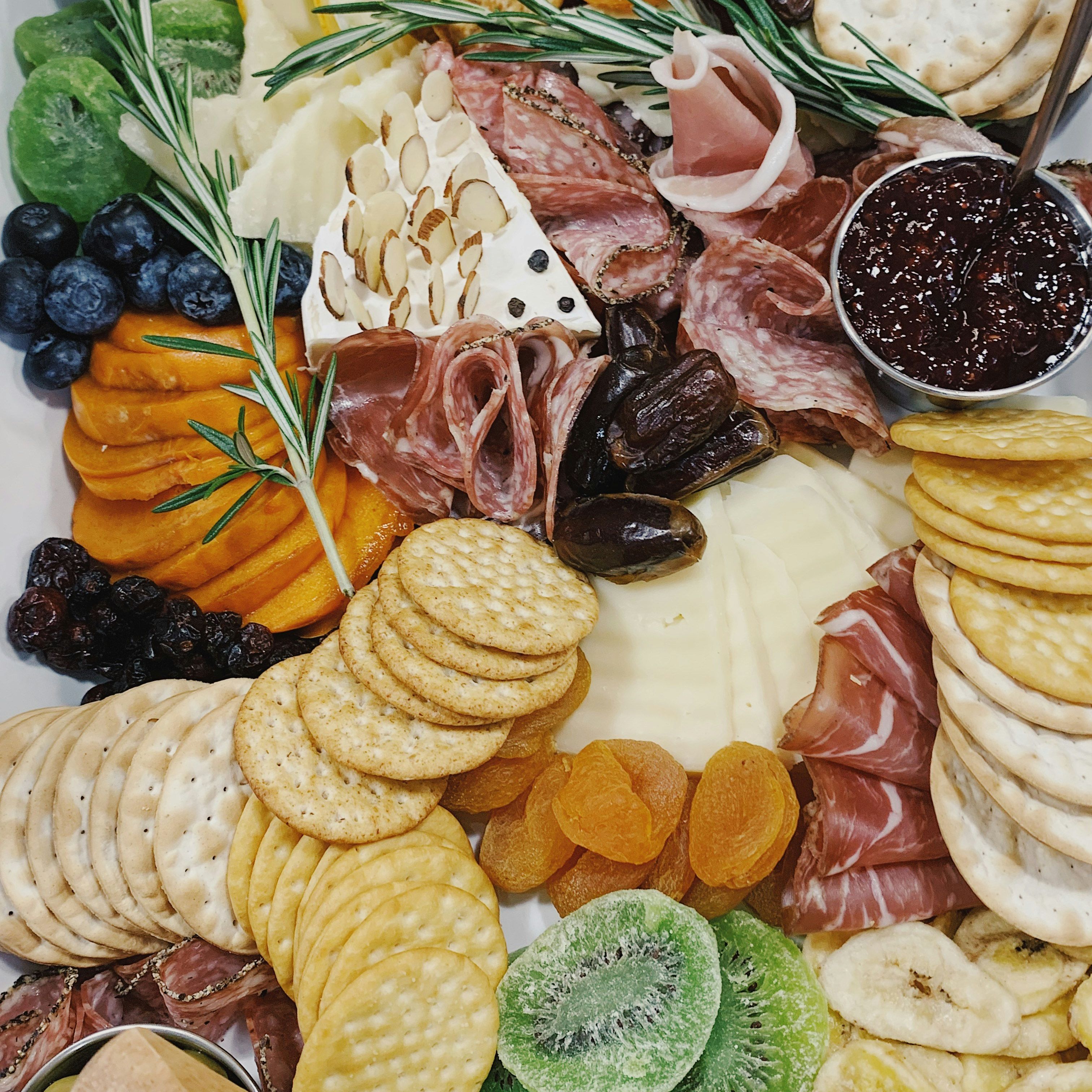 A charcuterie board with assorted crackers, cheeses, fruits, olives, nuts, and cured meats