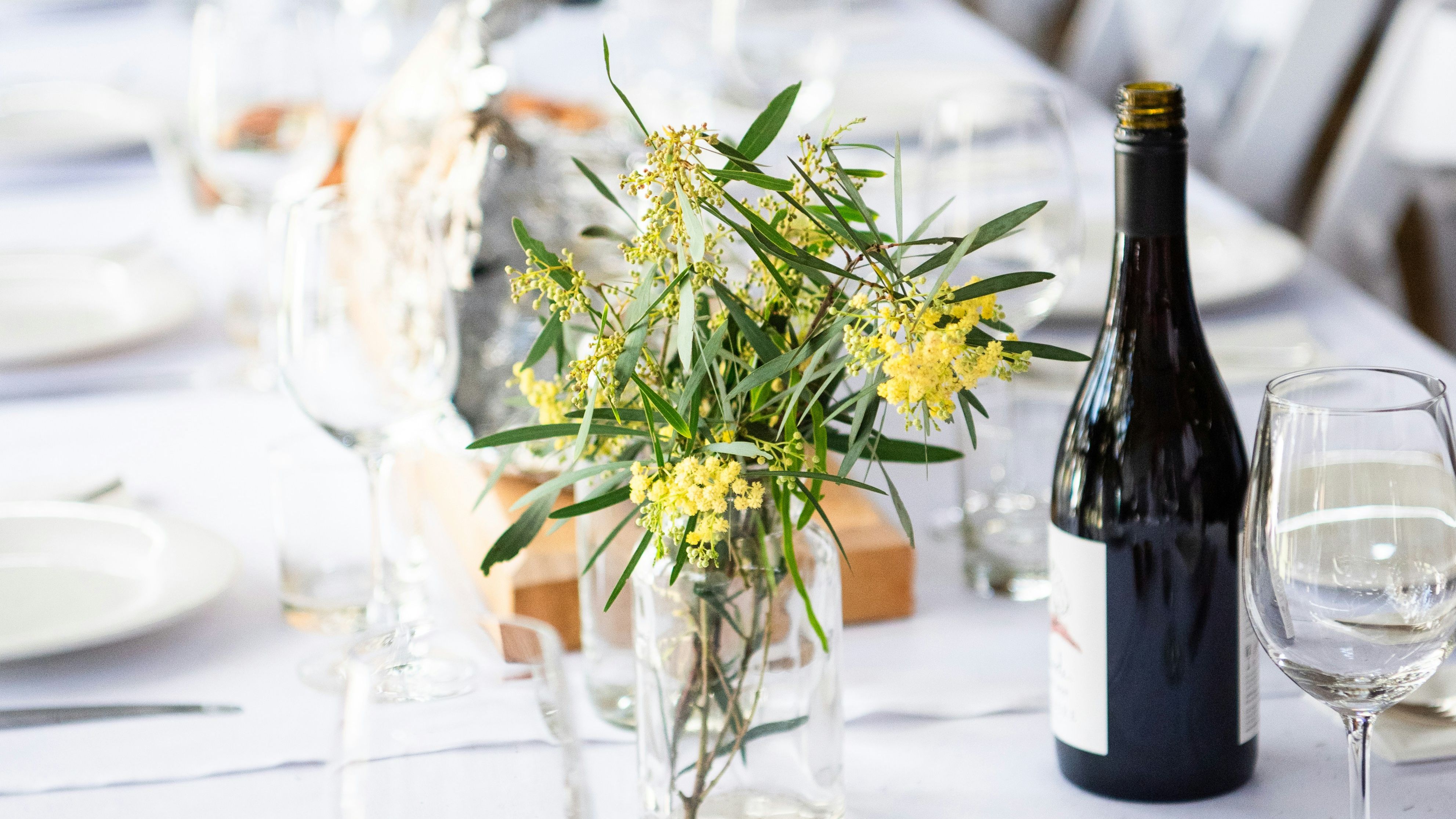 Elegant table setting with yellow flowers, wine bottle, and glassware