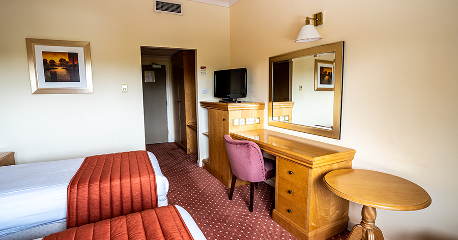 Hotel room with twin beds, wooden furniture, and a red carpet