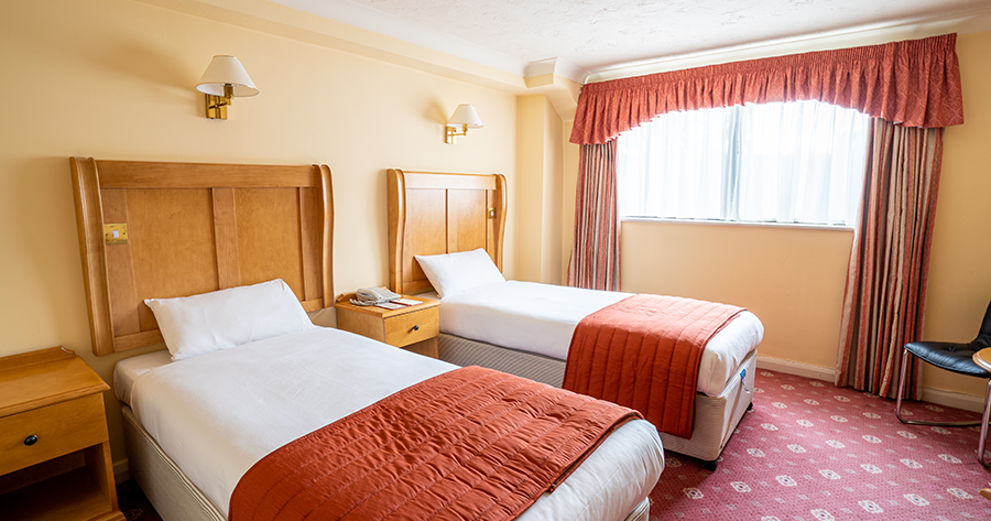 Hotel room with two single beds, wooden headboards, and orange bed covers