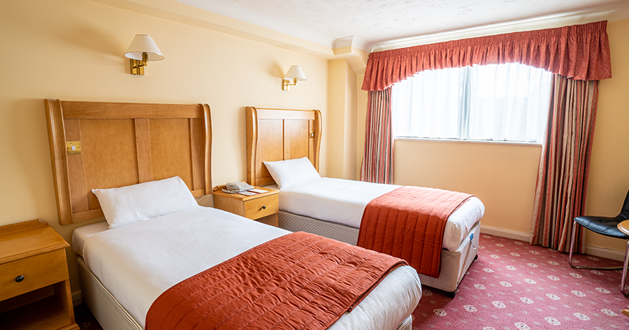 Hotel room with two single beds, orange bedding, and large window with orange curtains