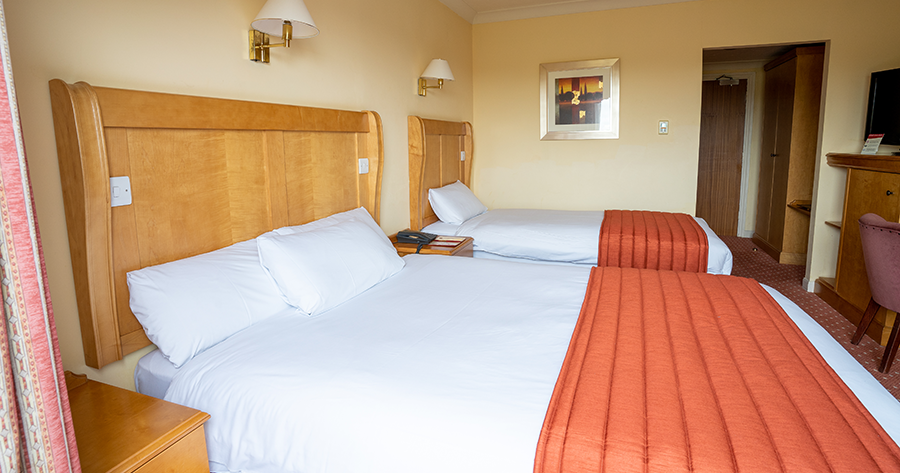 Hotel room with two beds, wooden headboards, and orange bed runners