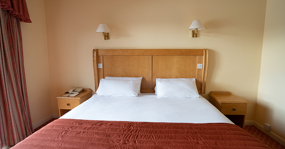 Hotel room with a double bed, wooden headboard, two pillows, and bedside tables.