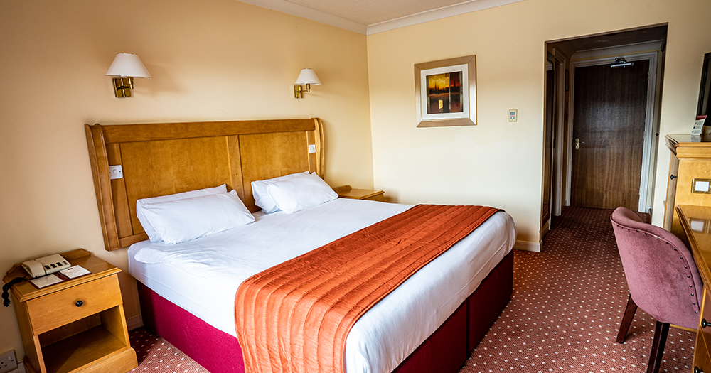 Hotel room with a double bed, wooden headboard, nightstand, and desk