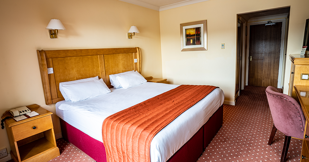Hotel room with a double bed, wooden headboard, nightstand, and desk
