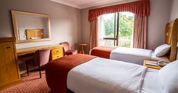 Hotel room with two single beds, a desk, mirror, and large window with curtains.