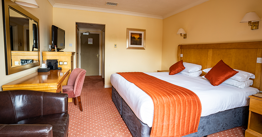 Well-lit hotel room with large bed and orange accents