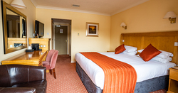 Hotel room with a double bed, orange accents, and a desk