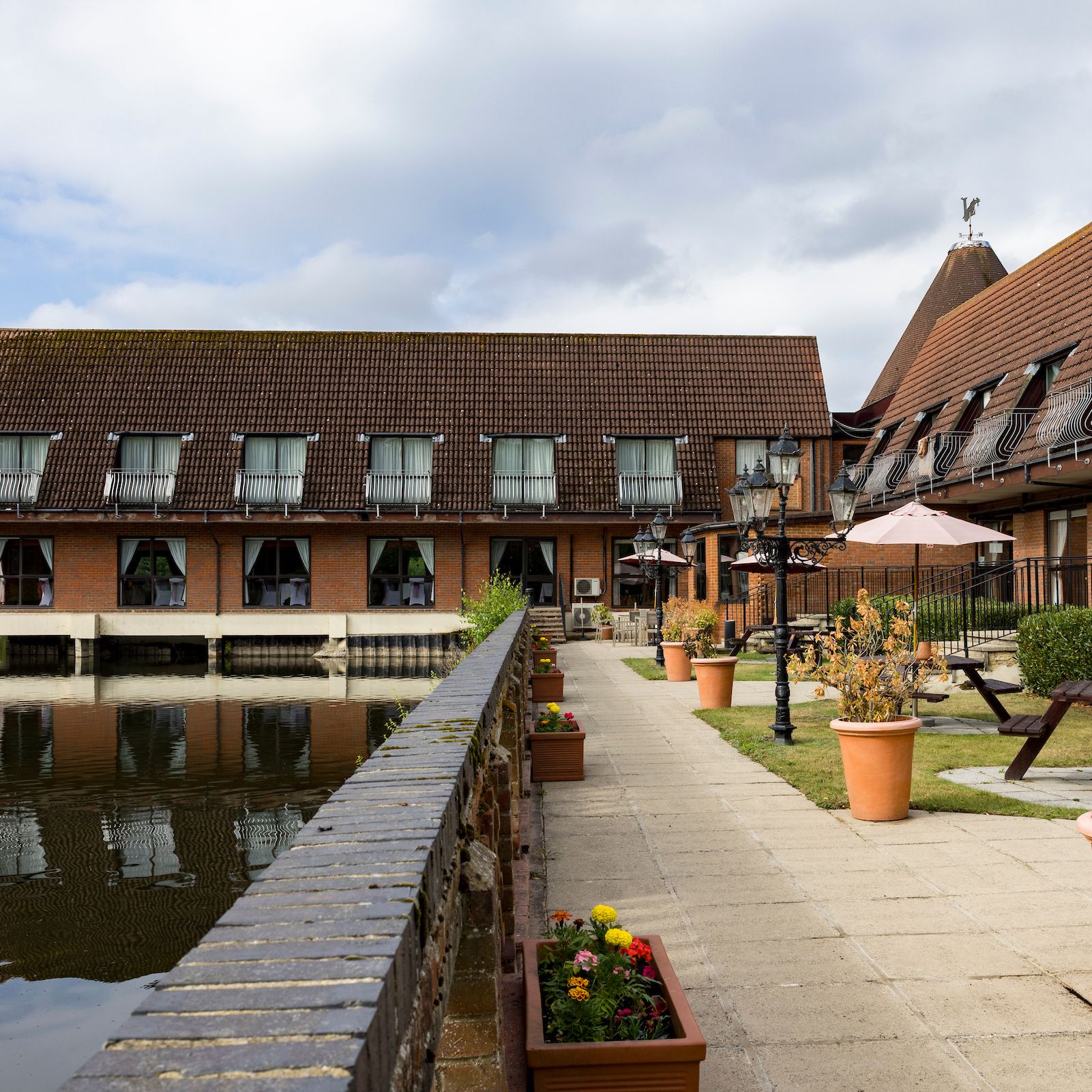 A lakeside hotel with outdoor seating and flower pots along a walkway beside the water.