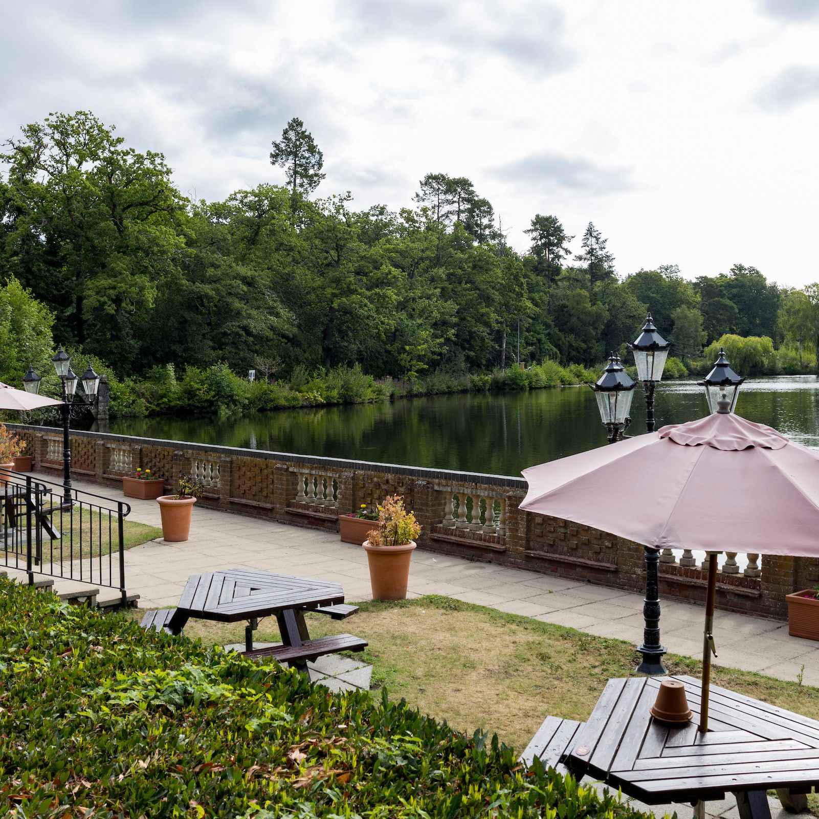 Outdoor seating area with umbrellas next to a lakeside and lush green trees