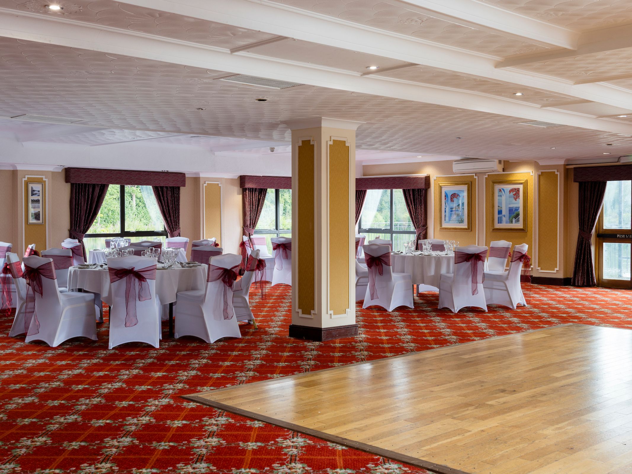Elegant banquet hall with round tables covered in white tablecloths and chairs decorated with burgundy bows.