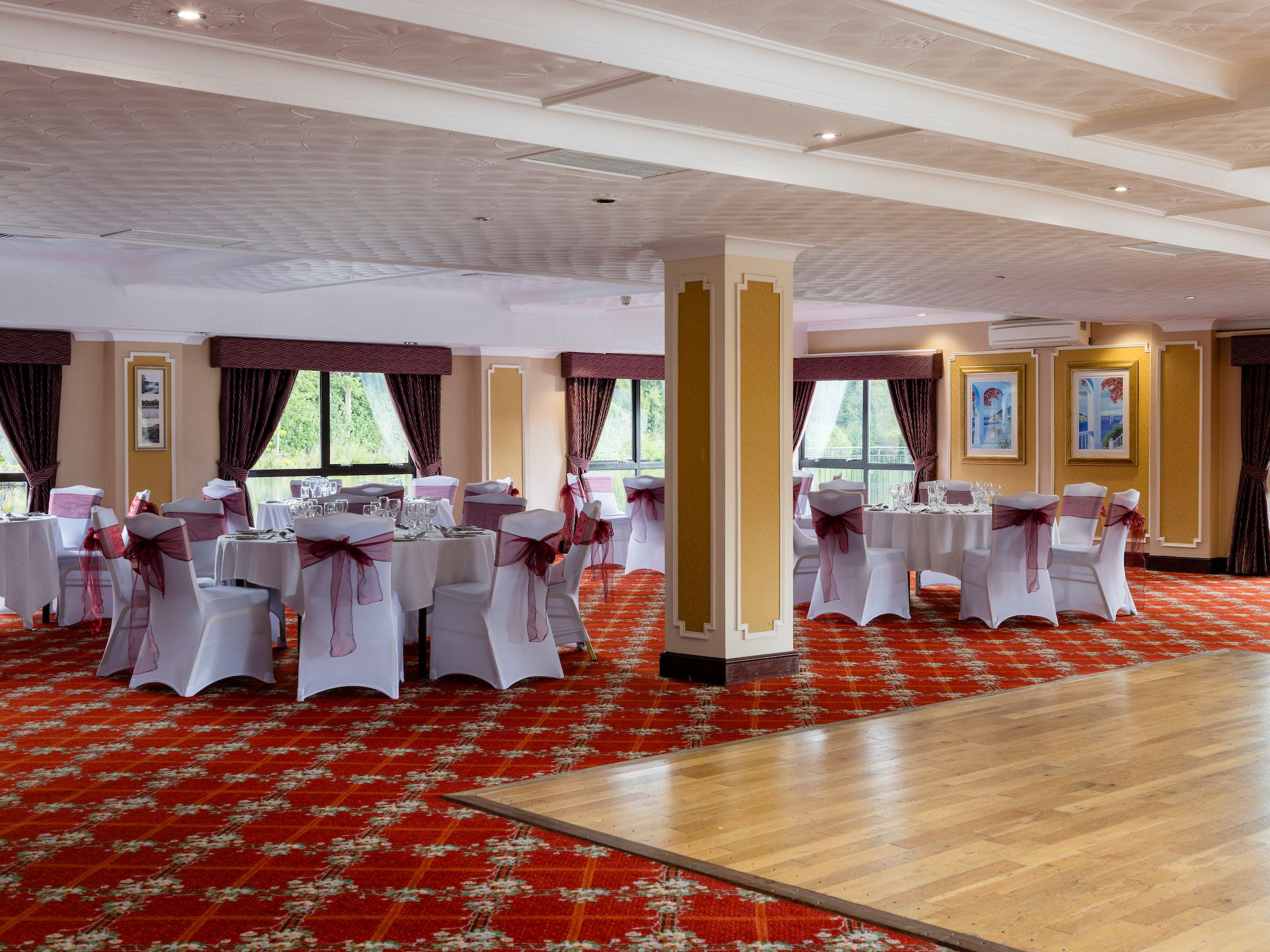 Elegant banquet hall with round tables covered in white tablecloths and chairs decorated with burgundy bows.
