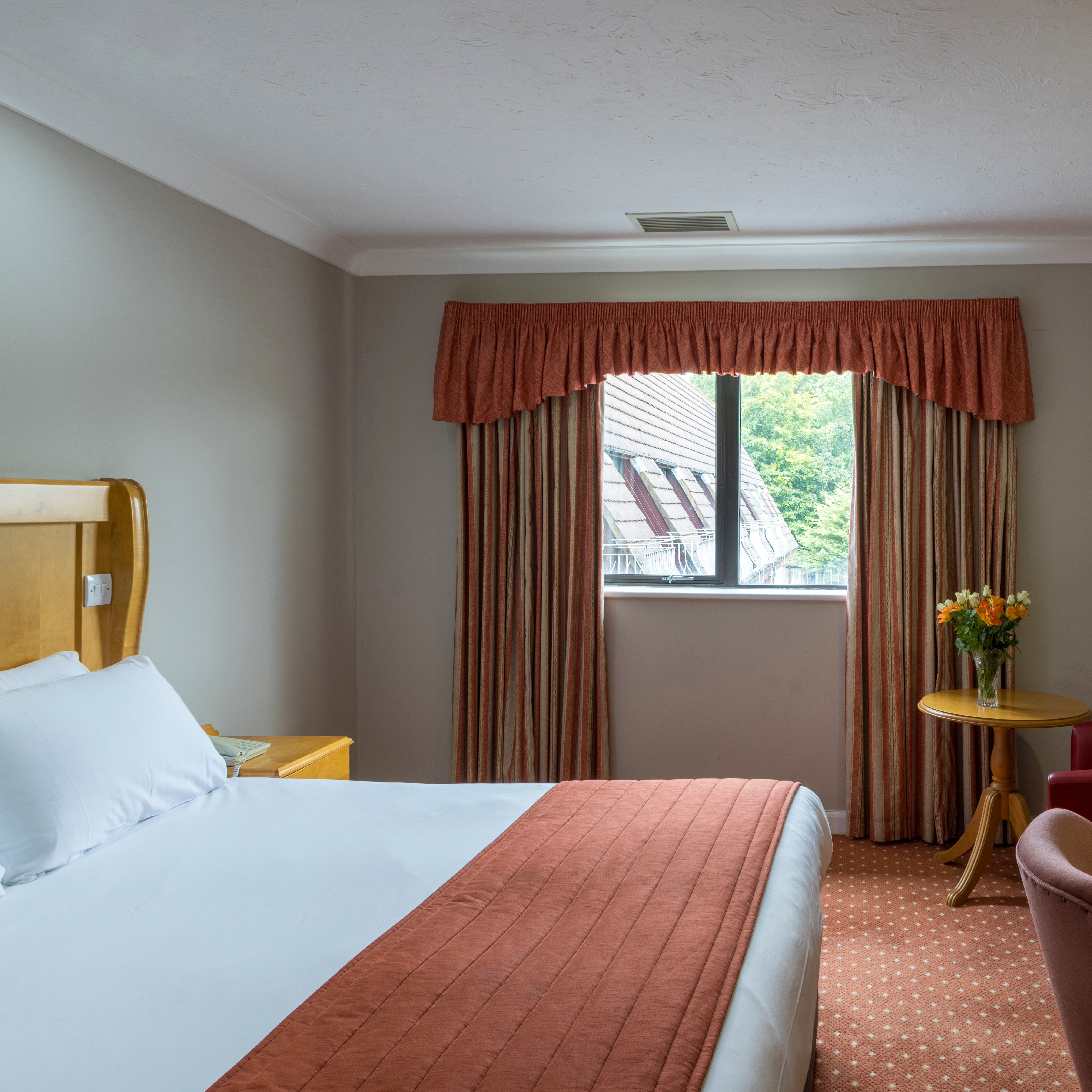A hotel room with a double bed, window with curtains, a desk, and a mirror.