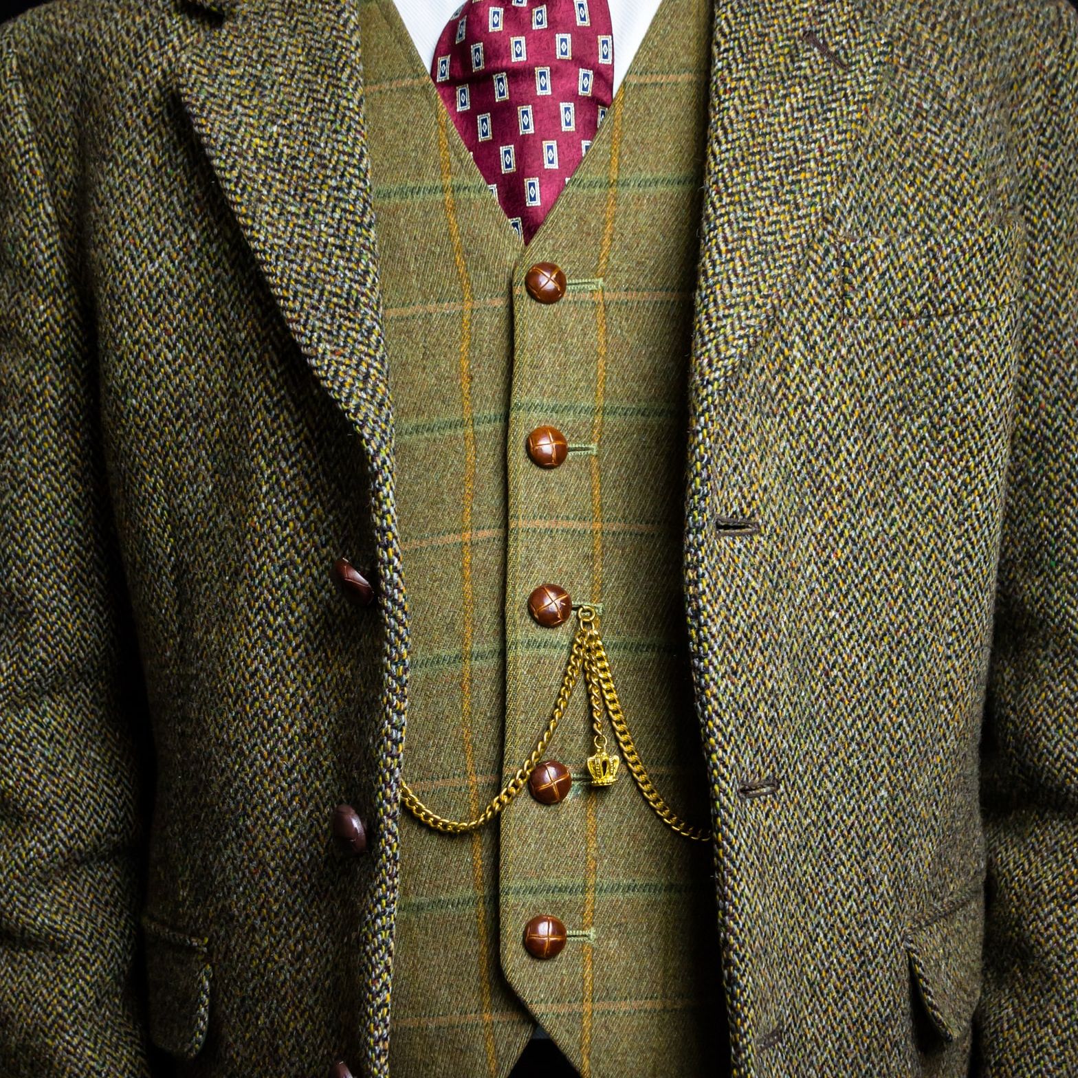 Man wearing a tweed suit with a patterned vest, red tie, and gold pocket watch chain
