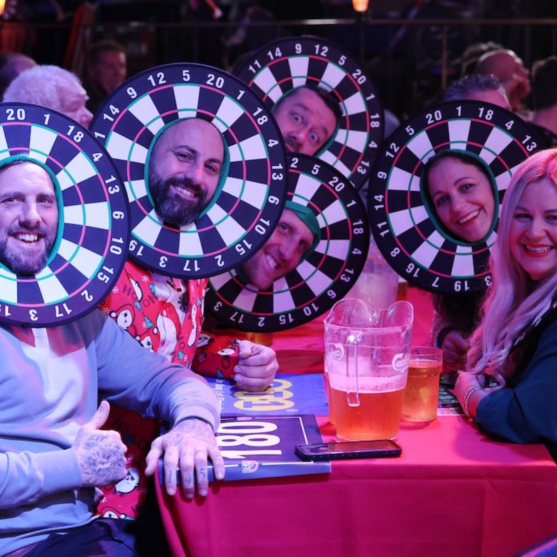 Group of people at a table wearing dartboard costumes around their faces, smiling and having fun.