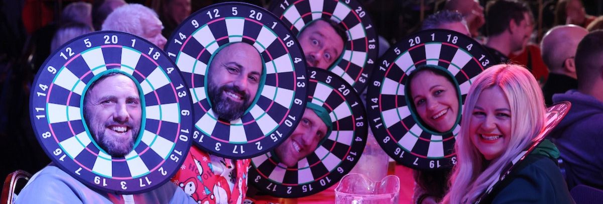 Group of people at a table wearing dartboard costumes around their faces, smiling and having fun.