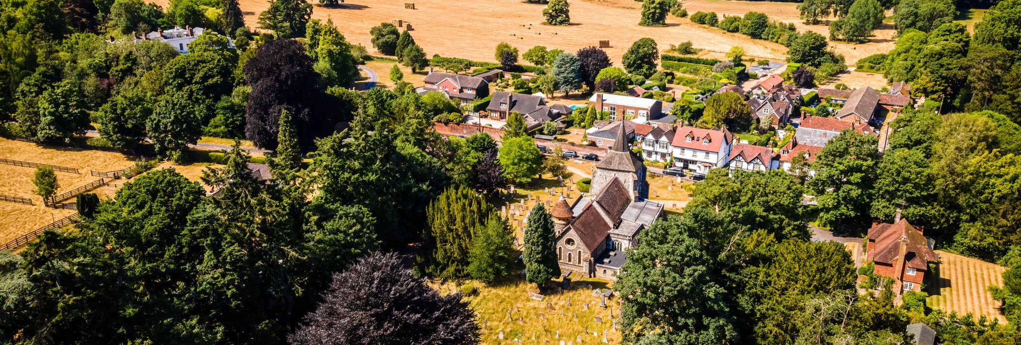 Aerial view of Mickleham, Surrey, showing a village with historic buildings, a church, and surrounding fields and woodland on a sunny day.