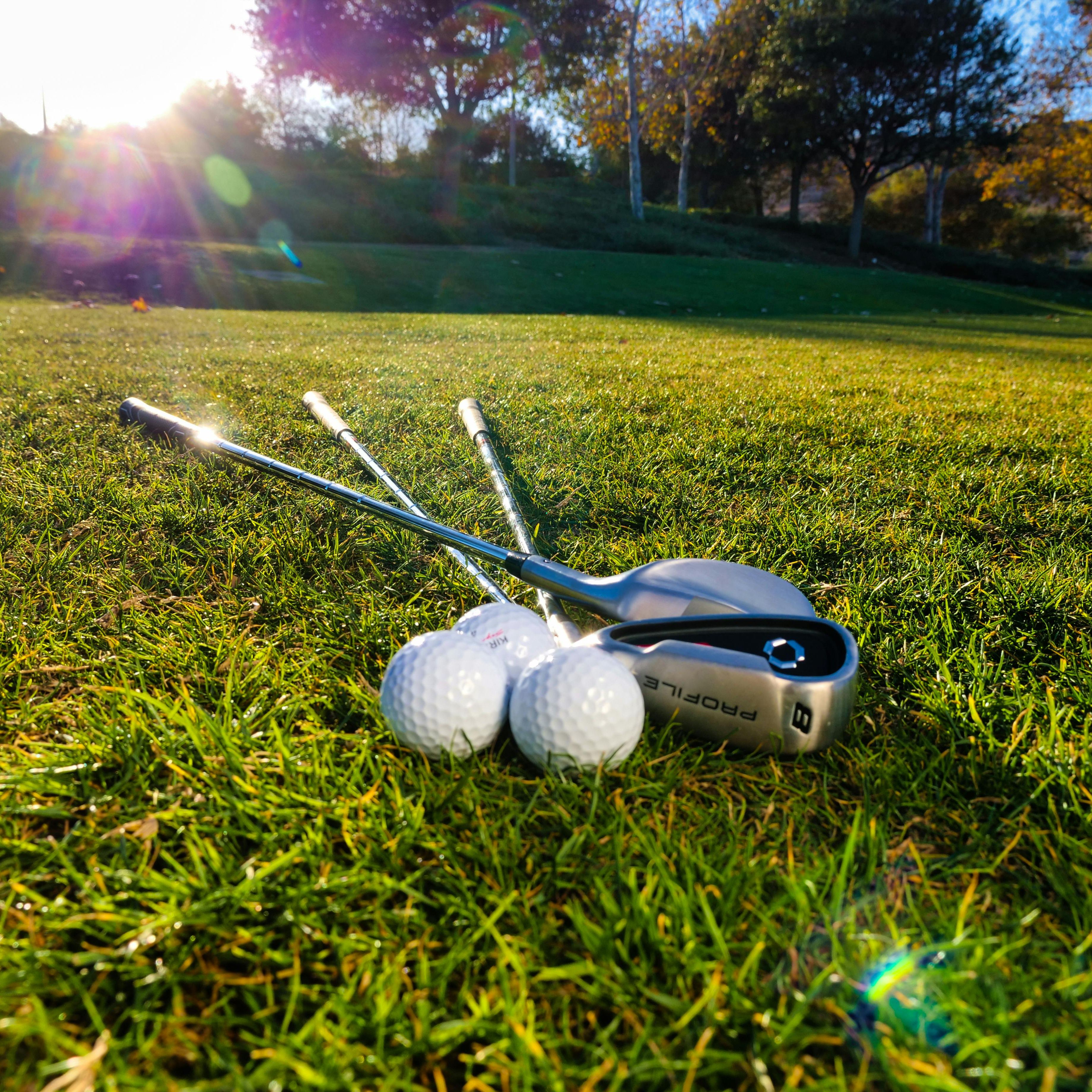 Golf clubs and golf balls on a grassy field with sunlight in the background