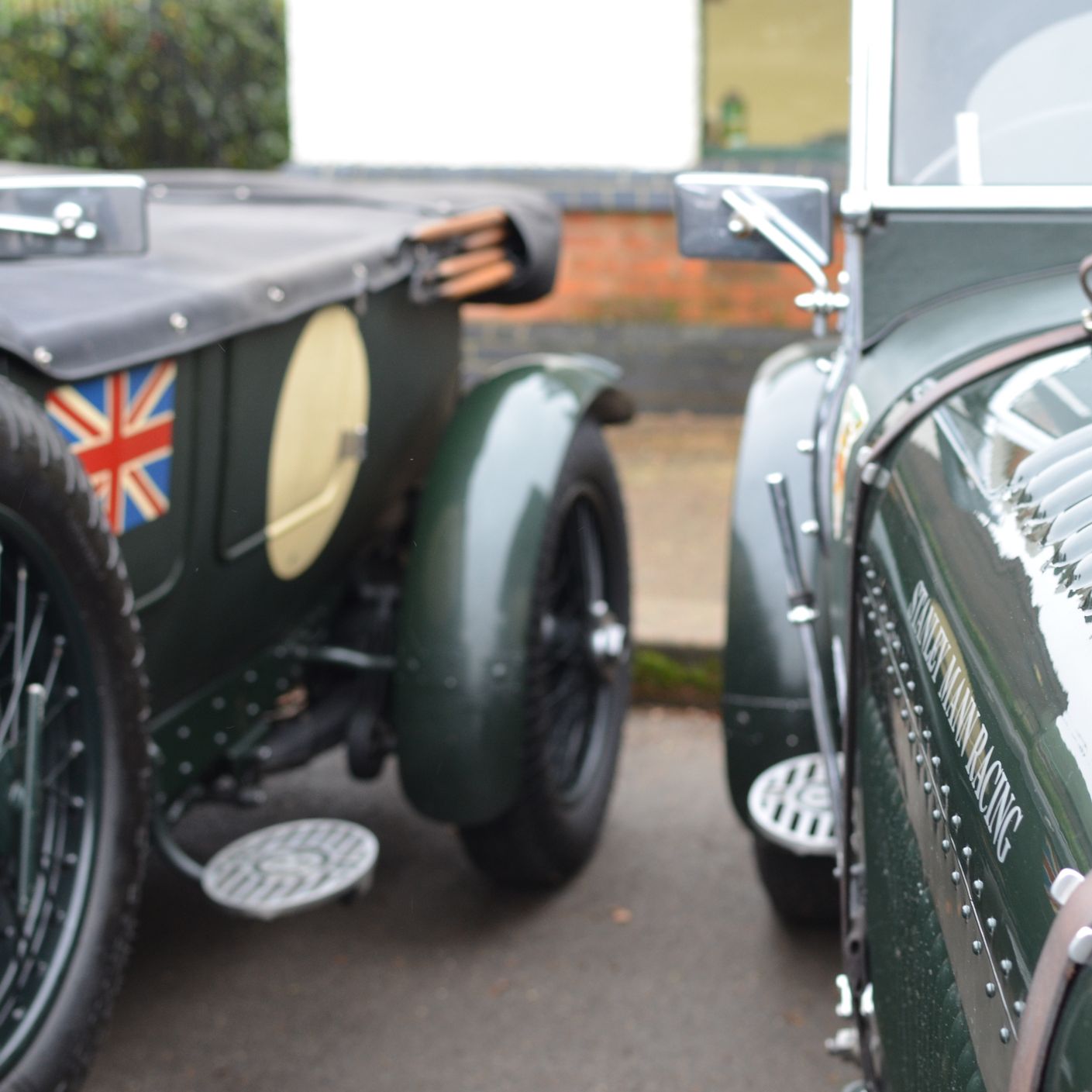 Close-up of two vintage green racing cars, showing polished bodywork, wire wheels and a Union flag detail.