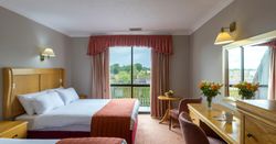 Hotel room with two double beds, a desk, flowers, and a large window with a view.
