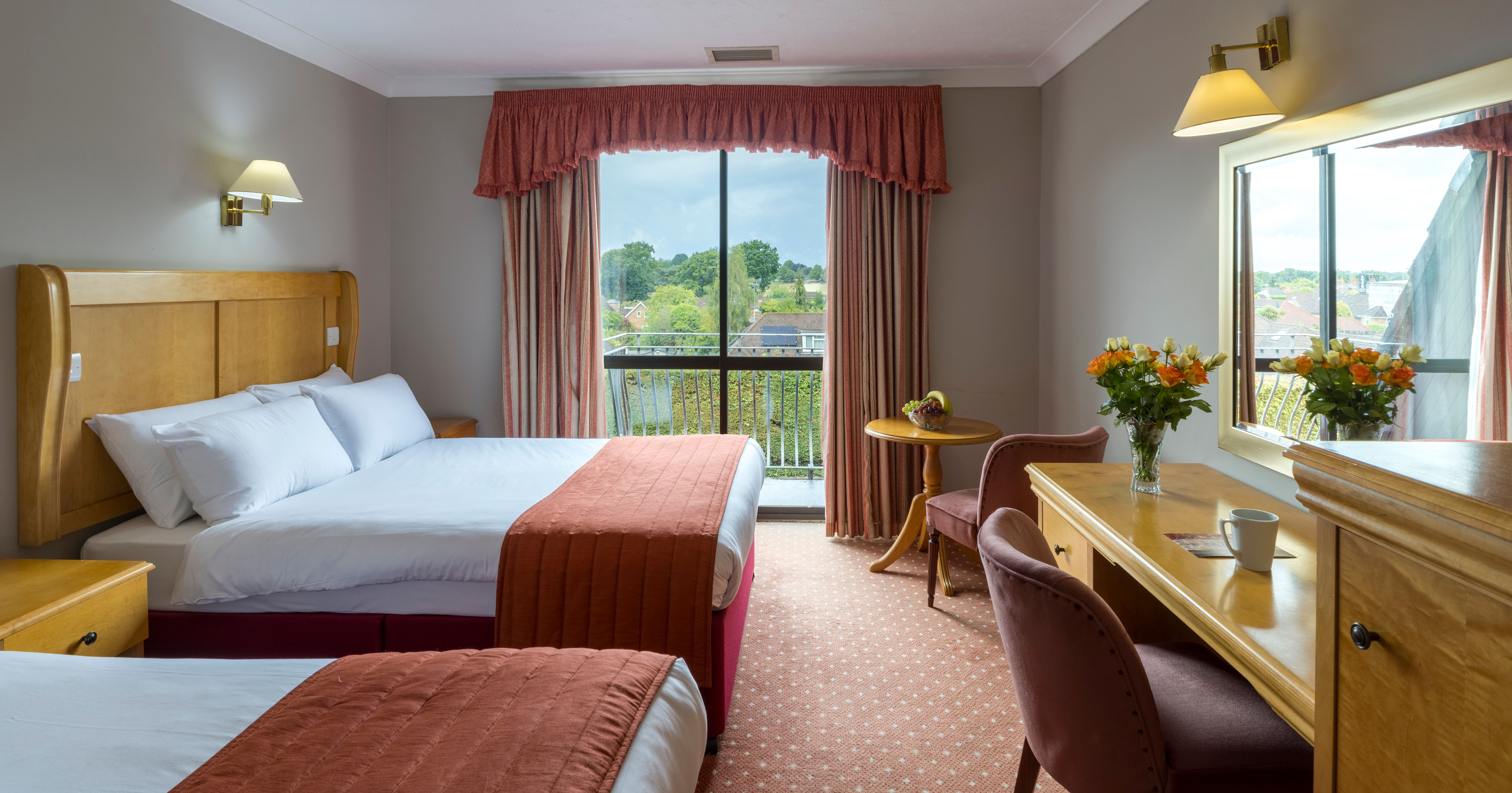 Hotel room with two double beds, a desk, flowers, and a large window with a view.