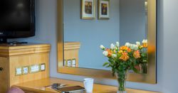 A desk with a vase of orange and white roses, a coffee cup, a tablet, and a smartphone, with a large mirror above.