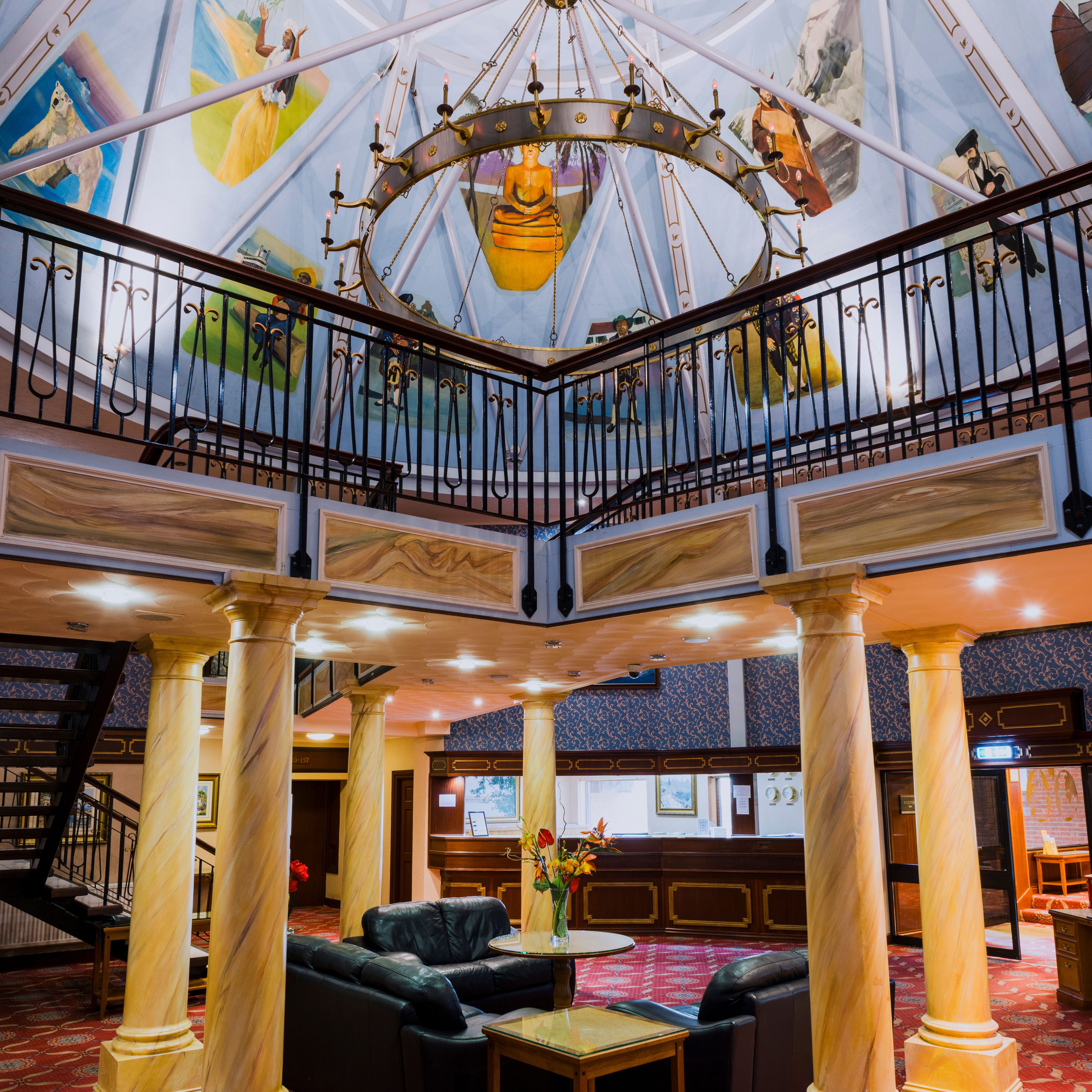 Luxurious hotel lobby with classical columns, seating area, and a painted dome ceiling with a chandelier.