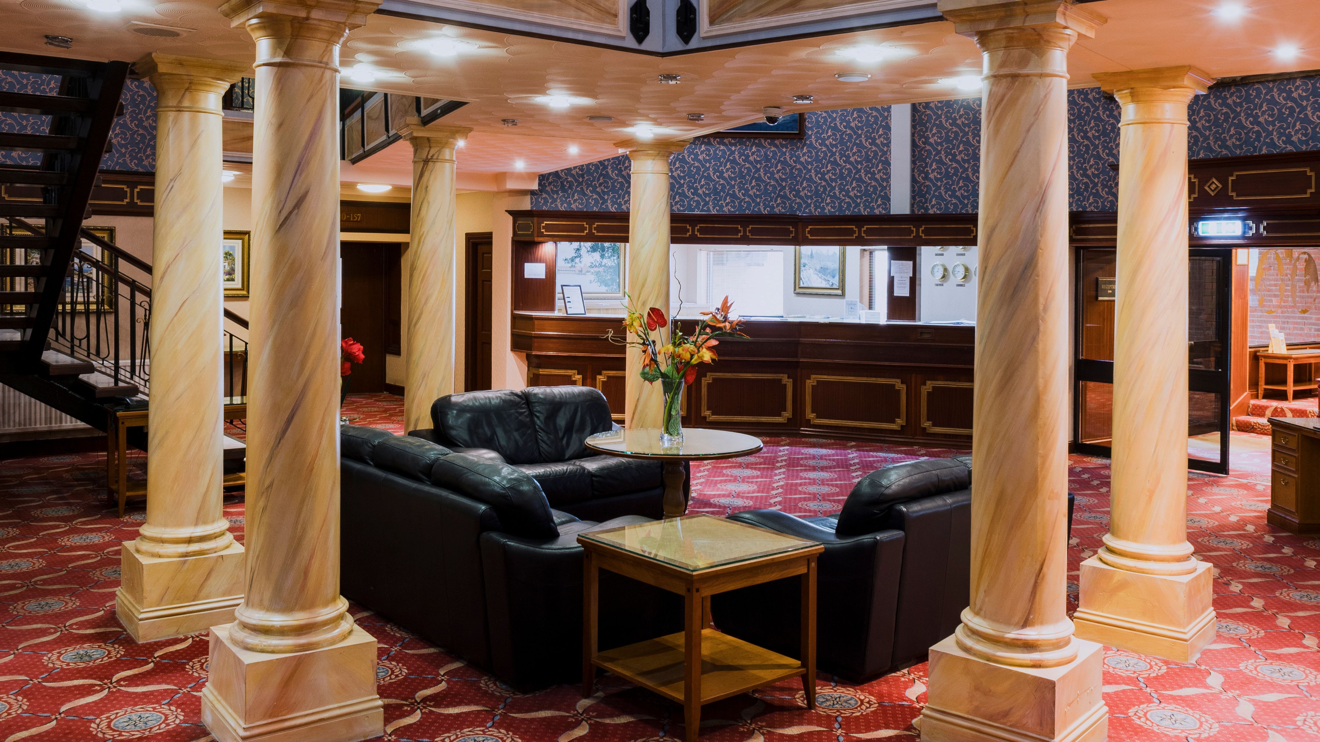Hotel lobby with marble columns, black leather sofas, and a reception desk in the background.