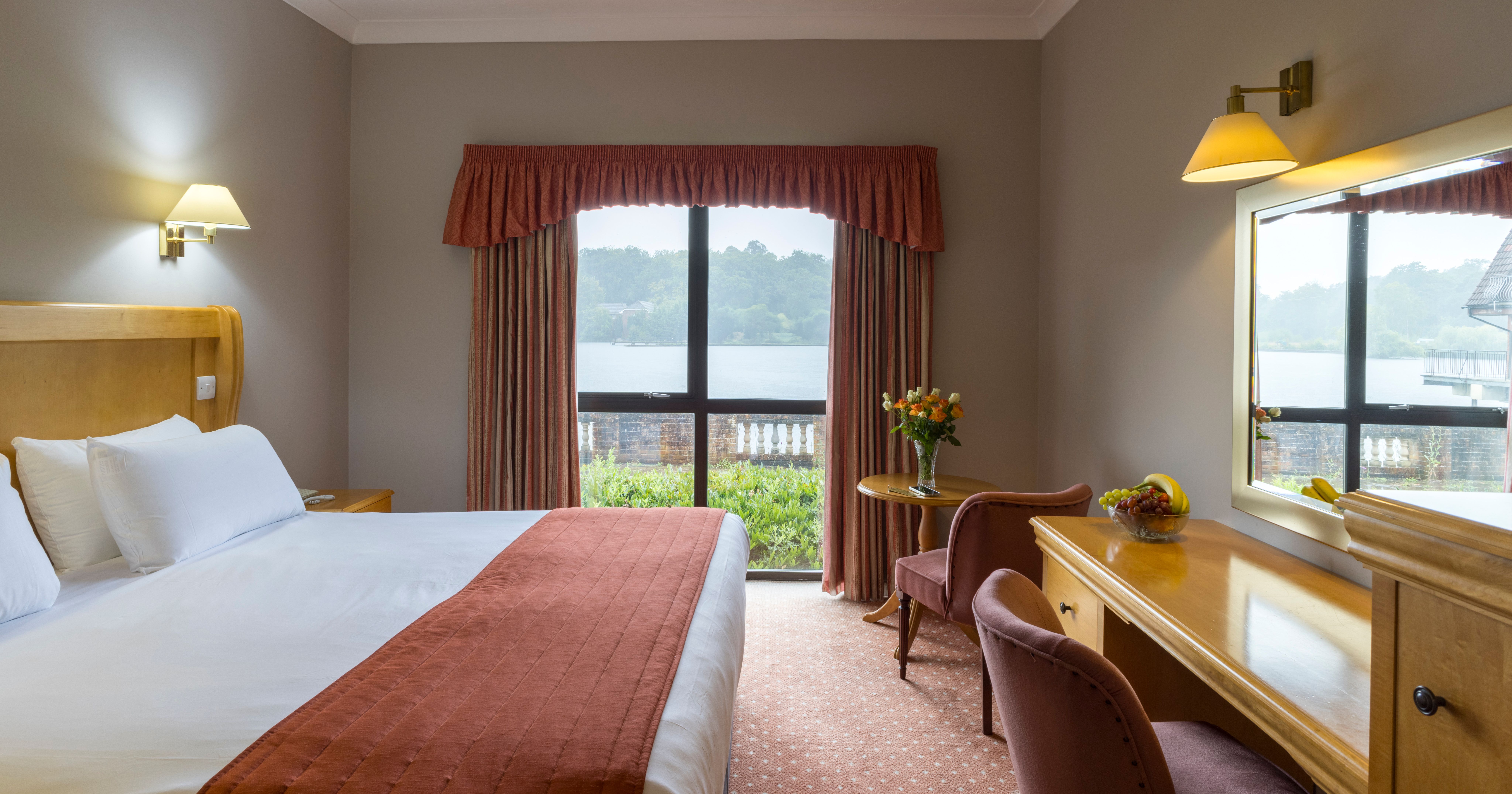 Cozy hotel room with a large bed, desk, and window view of a lake and greenery.