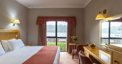 Cozy hotel room with a large bed, desk, and window view of a lake and greenery.