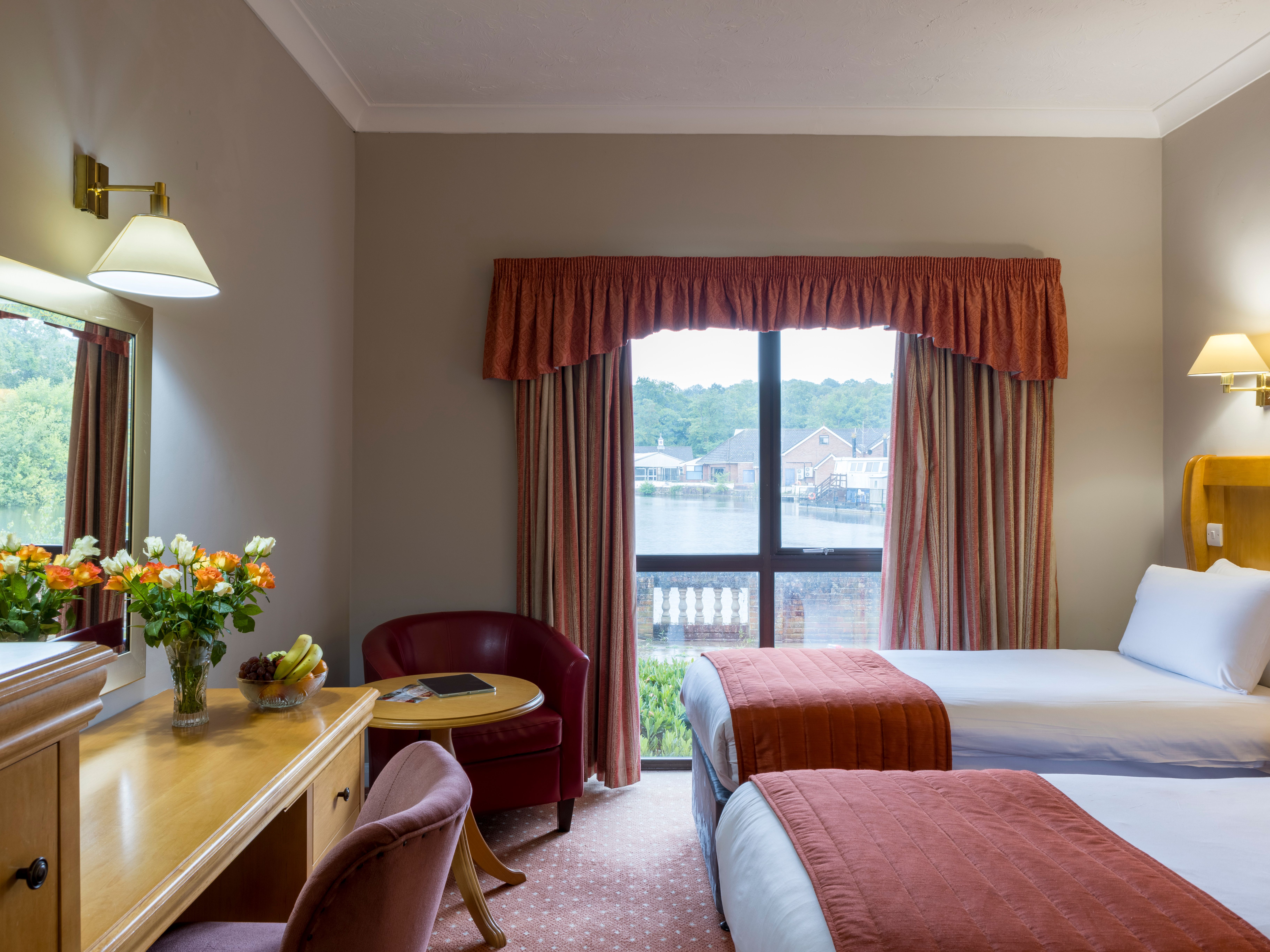Hotel room with two beds, a window view, desk, flowers, and armchairs