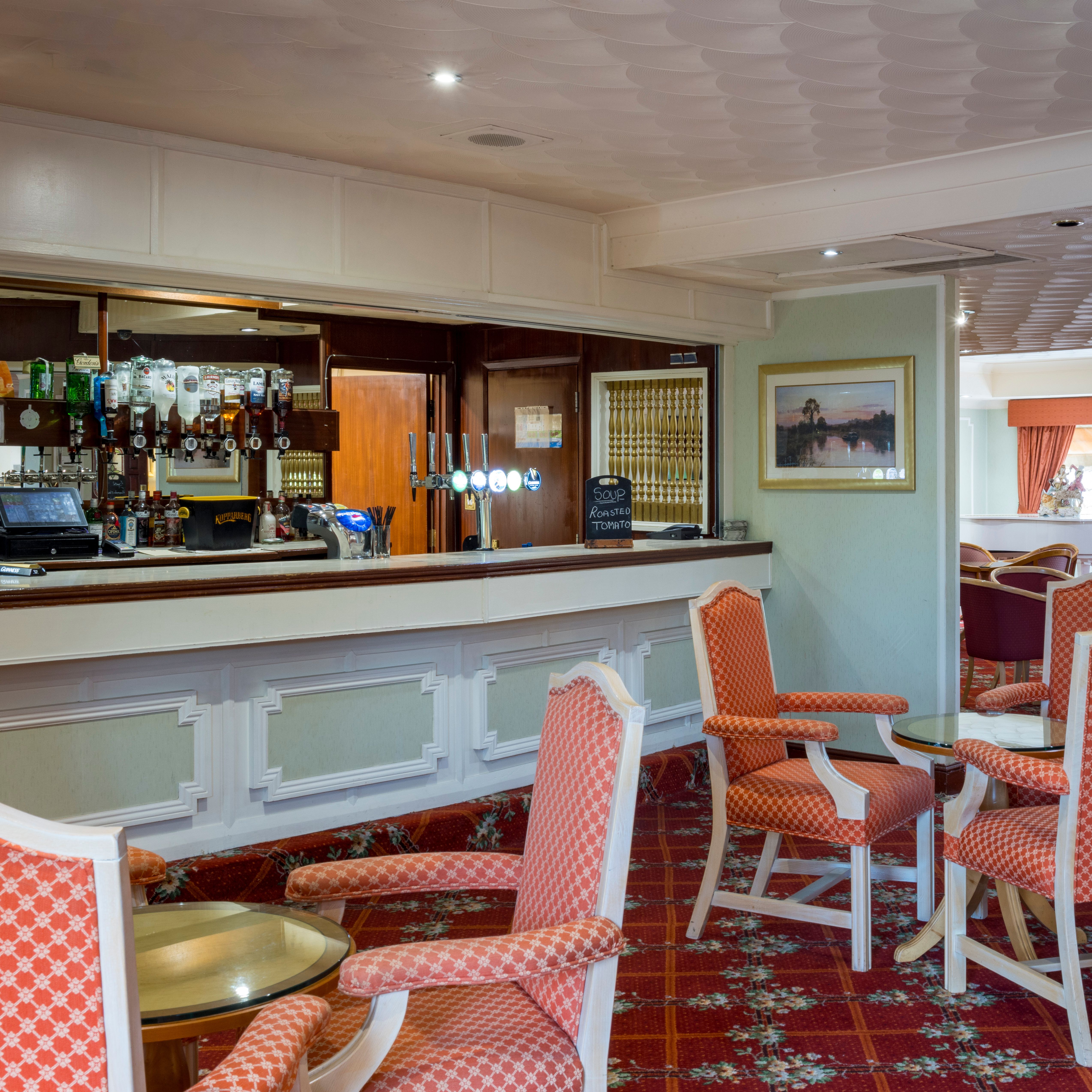 A cozy hotel lounge with a bar, red patterned chairs, and carpet.