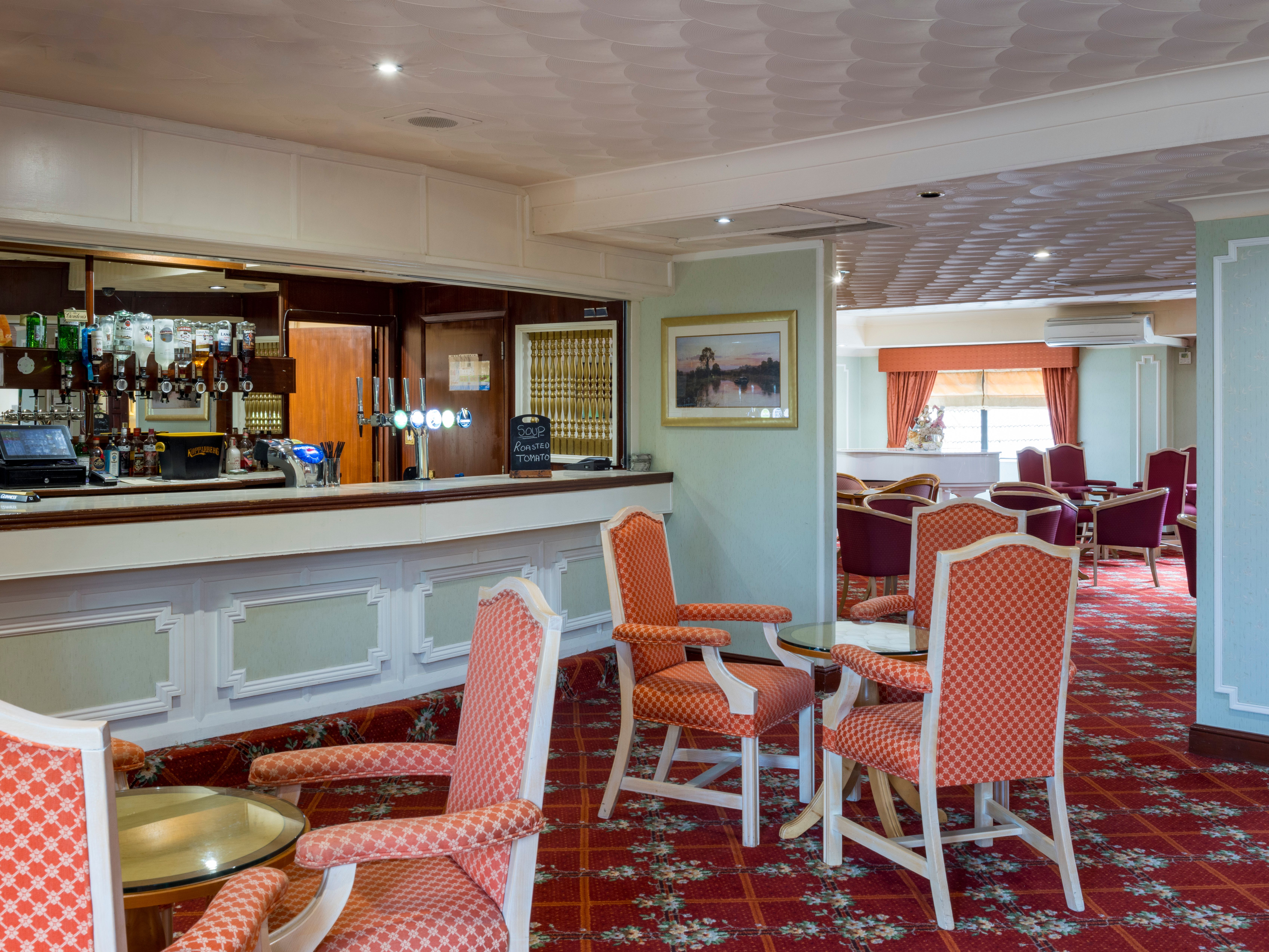 A cozy hotel lounge with a bar, red patterned chairs, and carpet.
