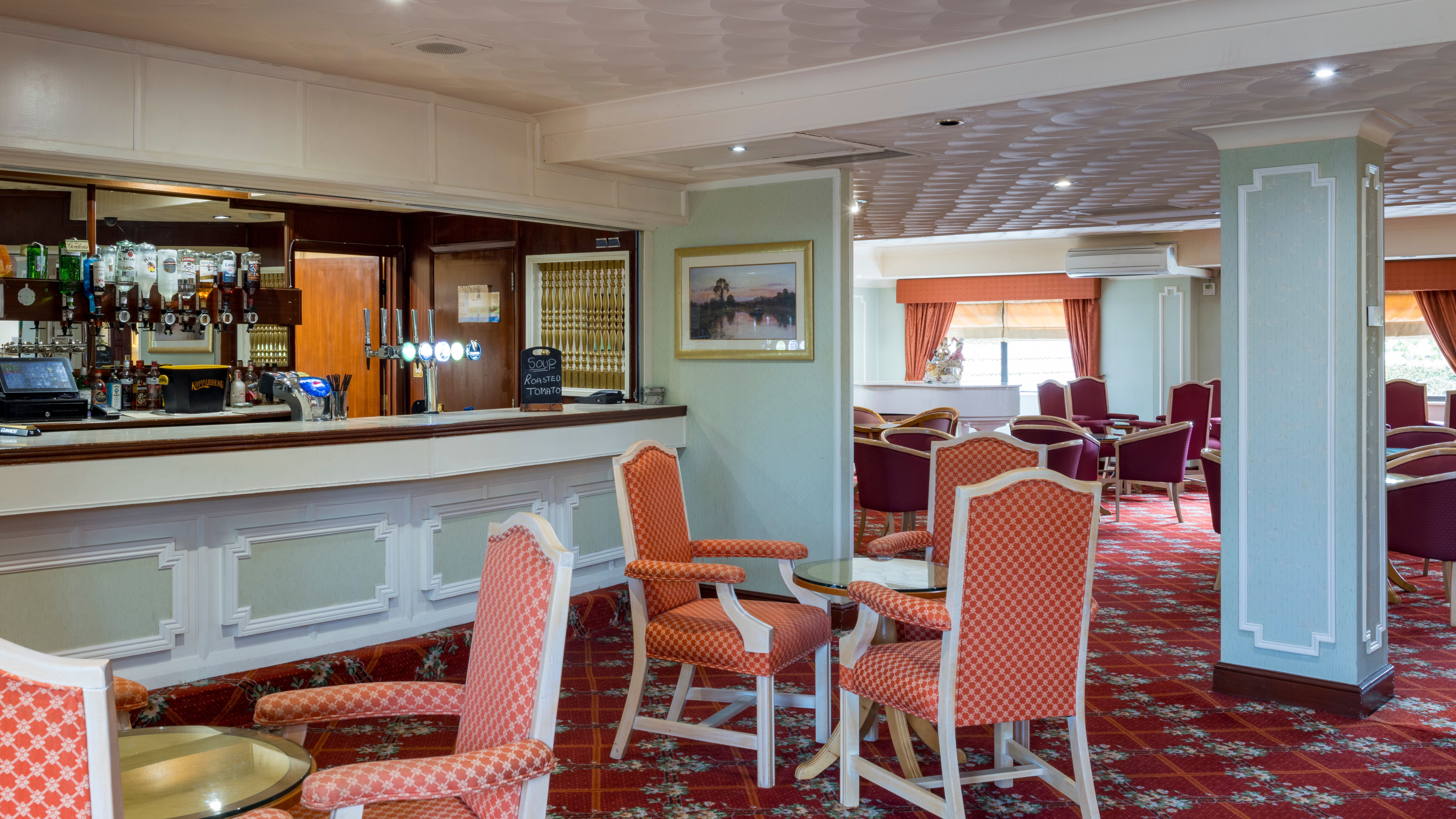 A cozy hotel lounge with a bar, red patterned chairs, and carpet.