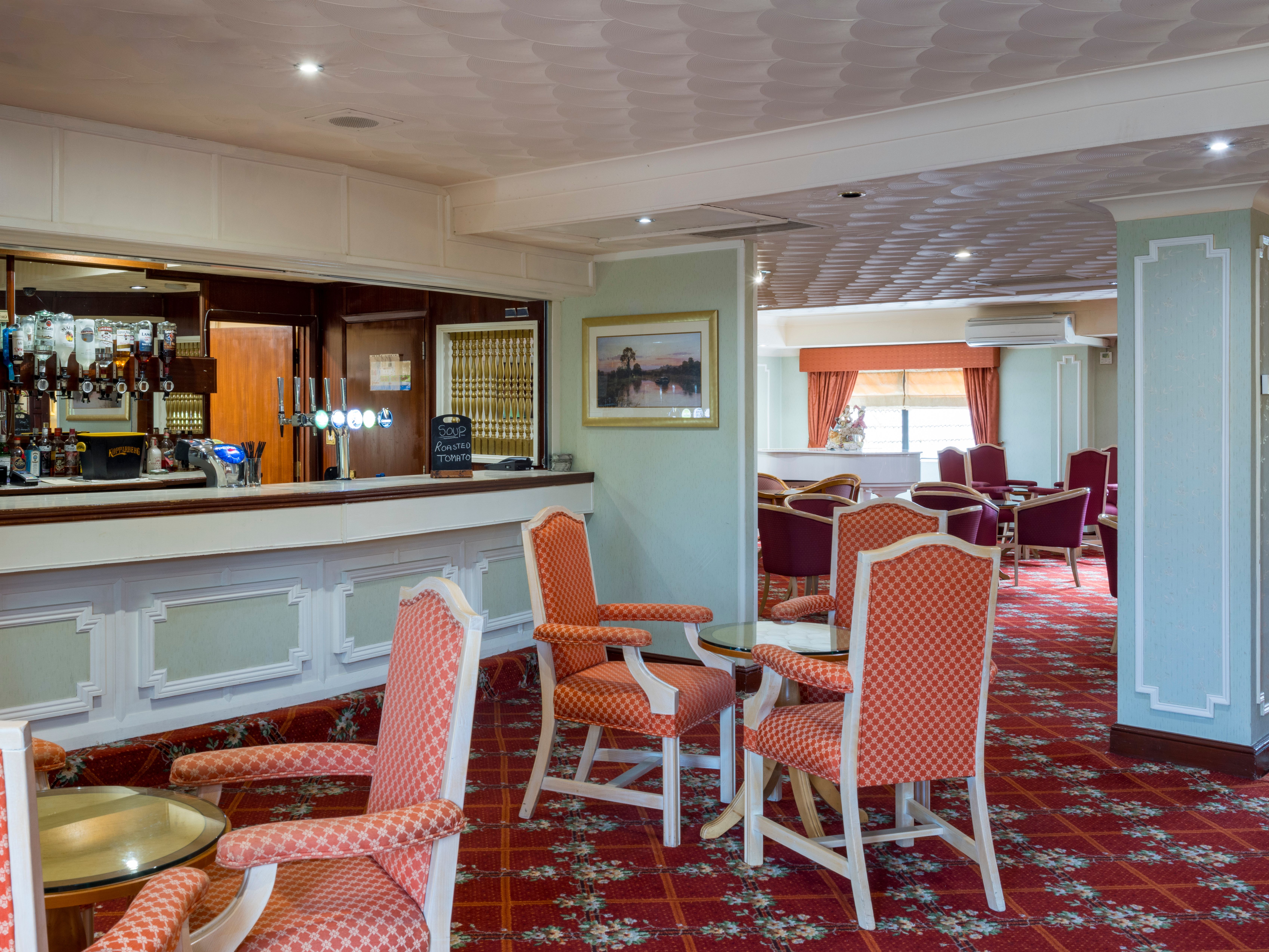A cozy hotel lounge with a bar, red patterned chairs, and carpet.