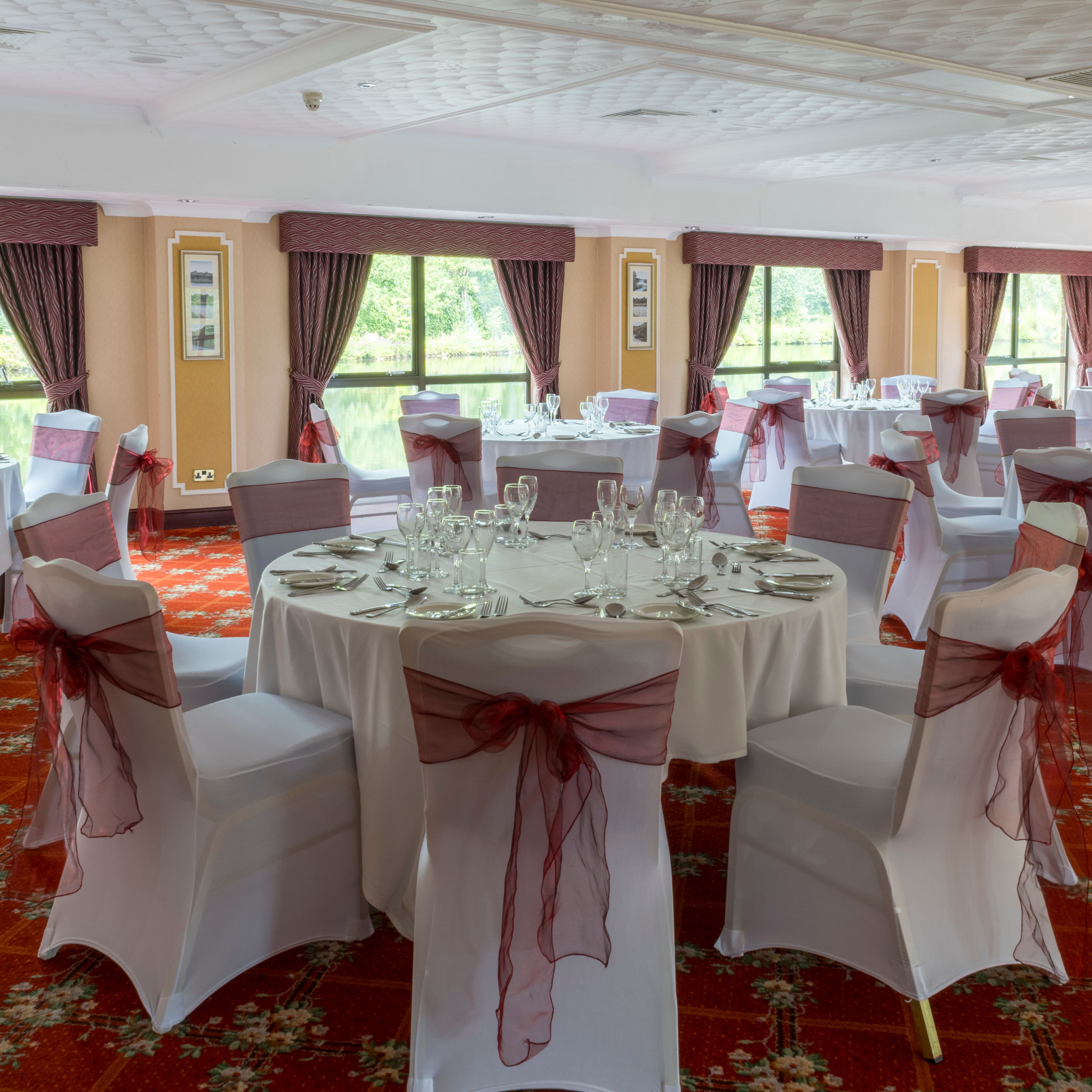 Elegant banquet hall set up for an event with round tables covered in white cloths and chairs adorned with burgundy sashes.