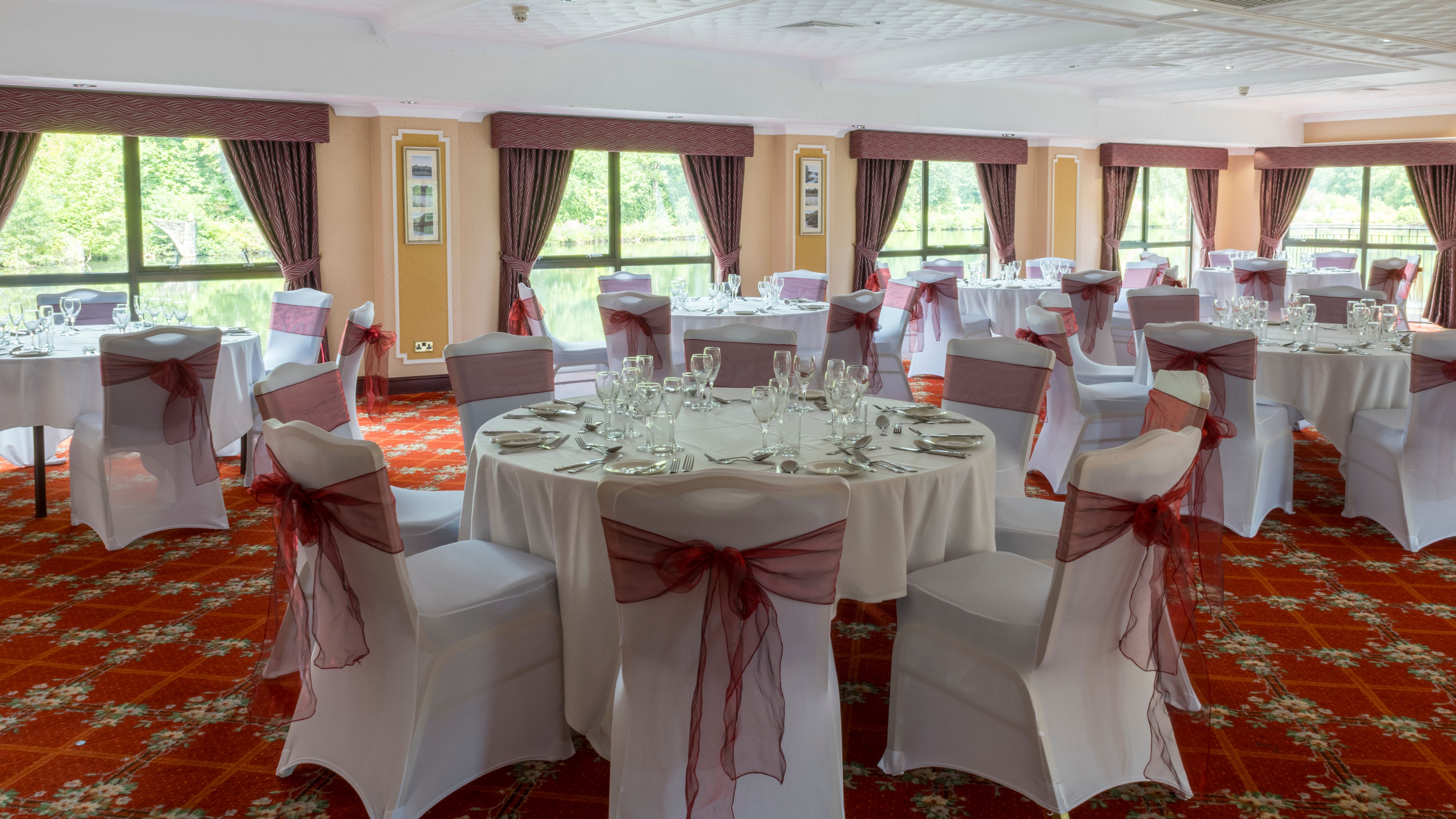 Elegant banquet hall set up for an event with round tables covered in white cloths and chairs adorned with burgundy sashes.