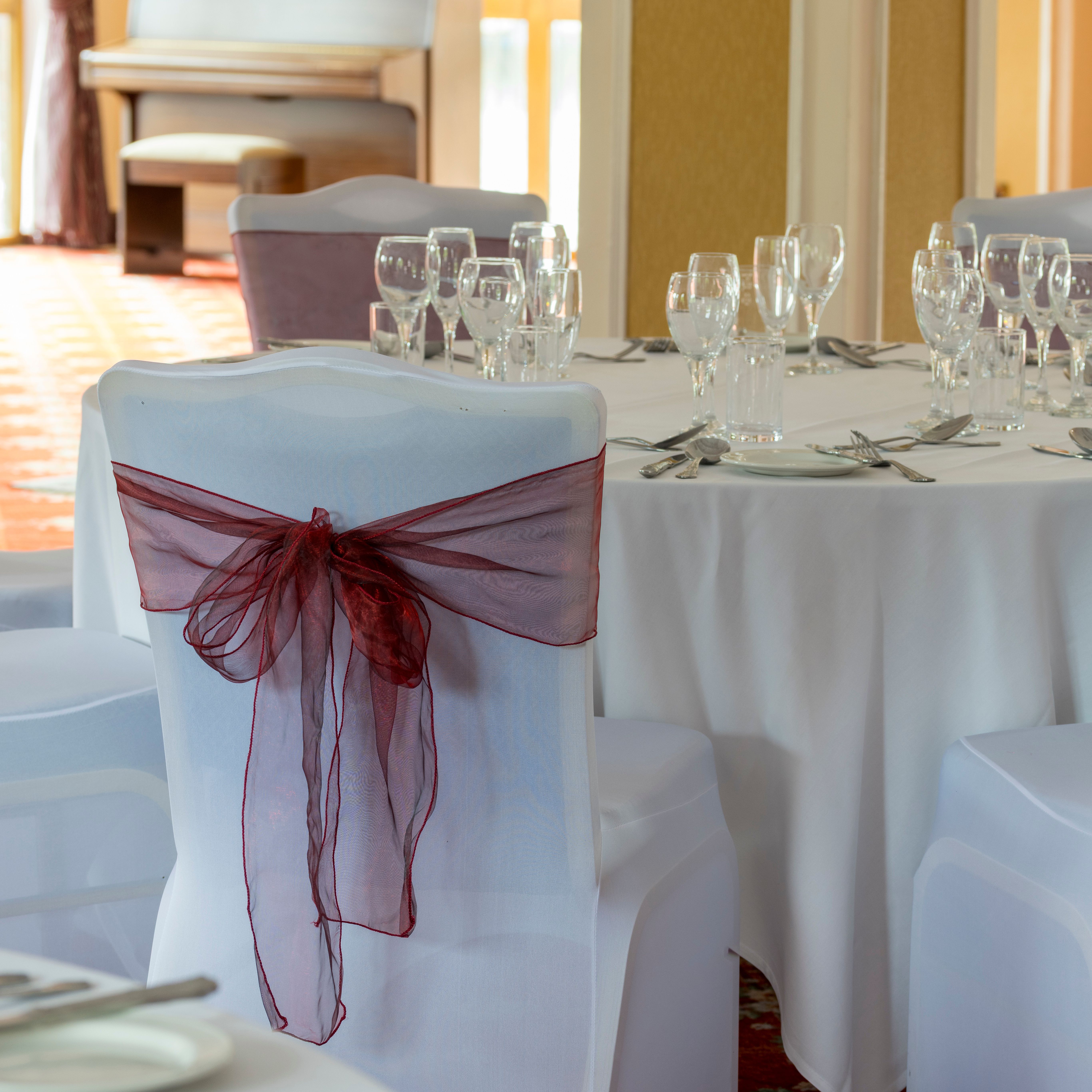 Elegant table setting with white tablecloth and chairs decorated with burgundy bows