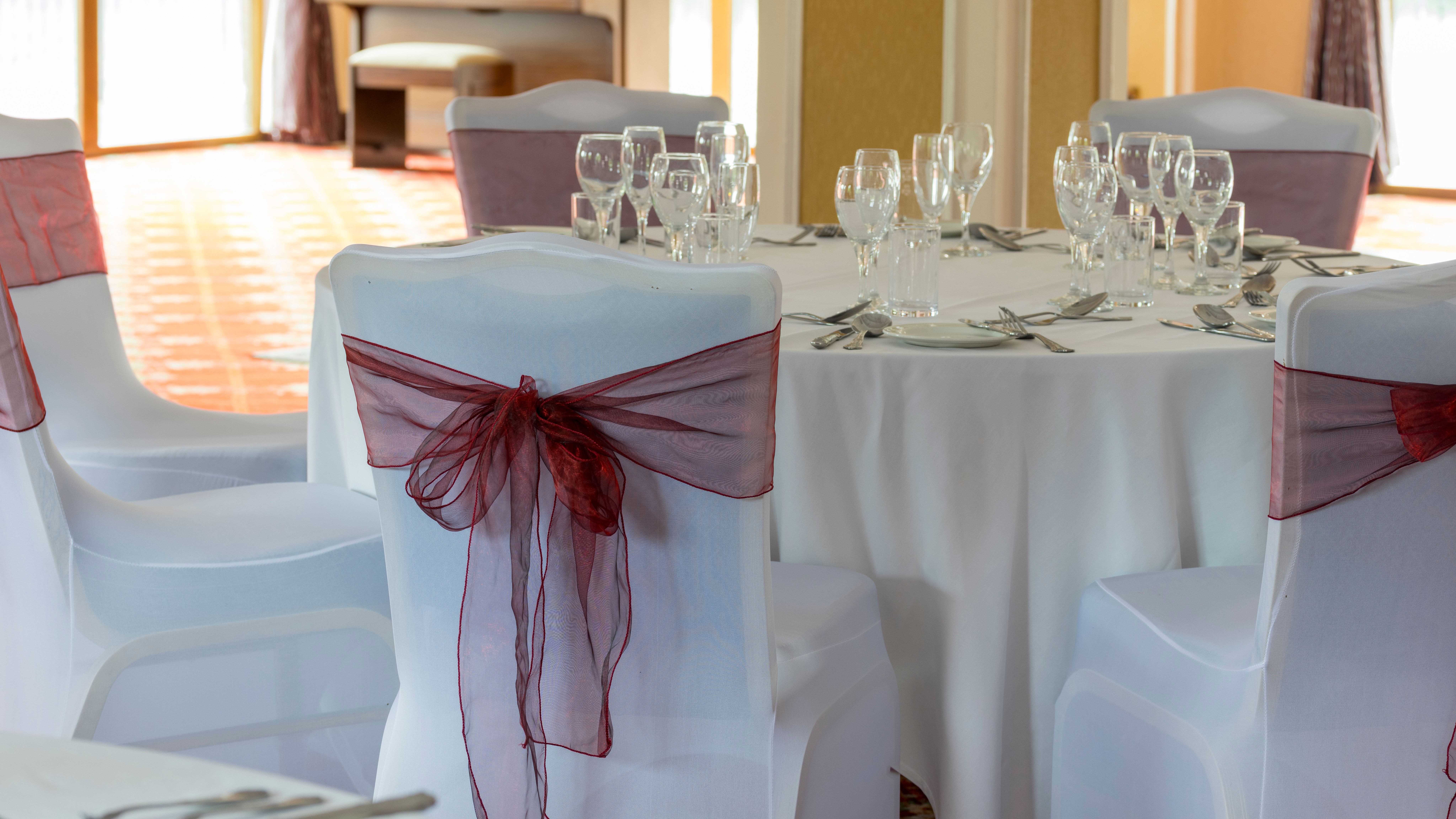 Elegant table setting with white tablecloth and chairs decorated with burgundy bows
