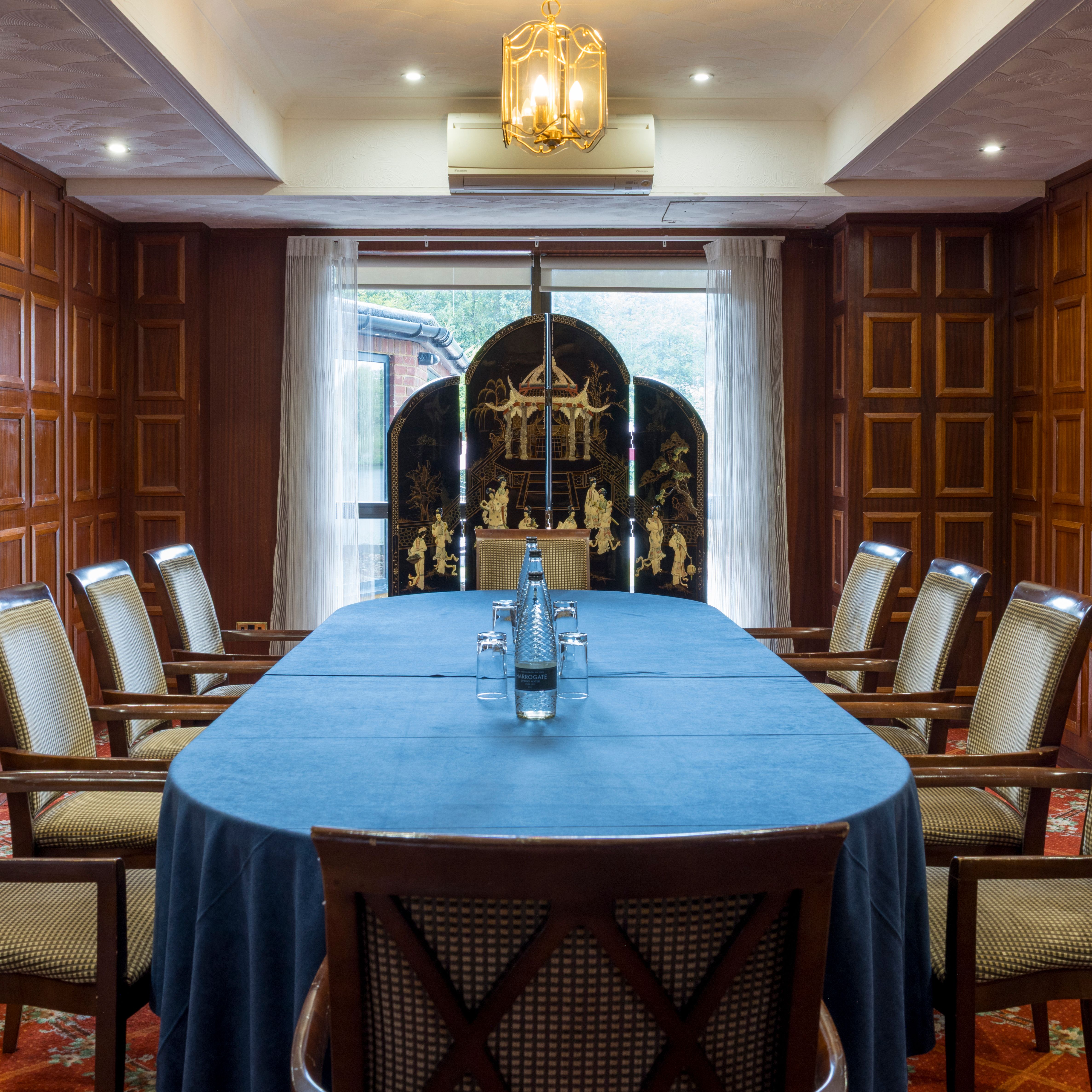 Elegant meeting room with wooden paneled walls, large blue-covered table, and cushioned chairs.
