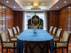 Elegant meeting room with wooden paneled walls, large blue-covered table, and cushioned chairs.