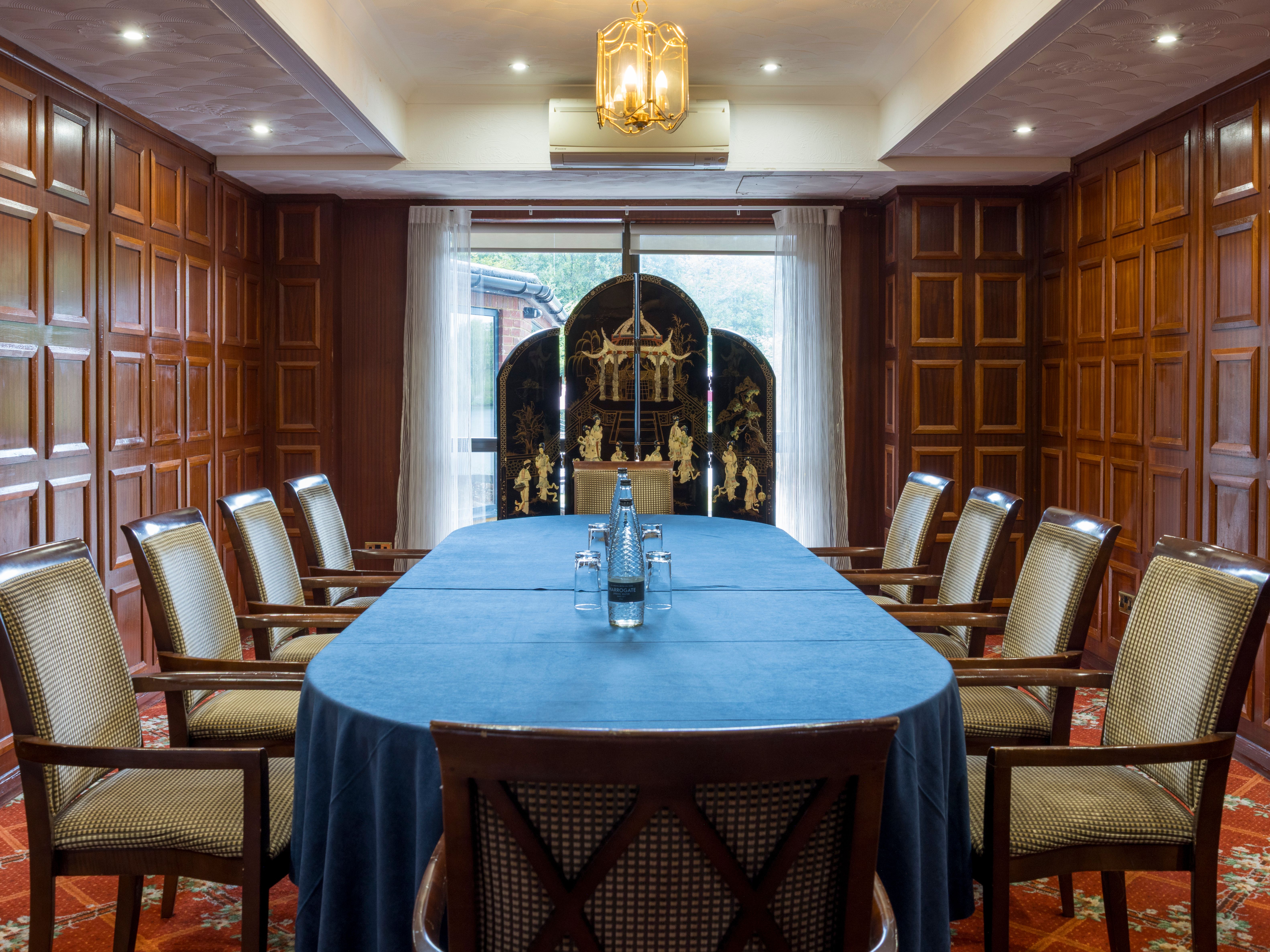 Elegant meeting room with wooden paneled walls, large blue-covered table, and cushioned chairs.