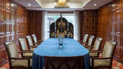 Elegant meeting room with wooden paneled walls, large blue-covered table, and cushioned chairs.