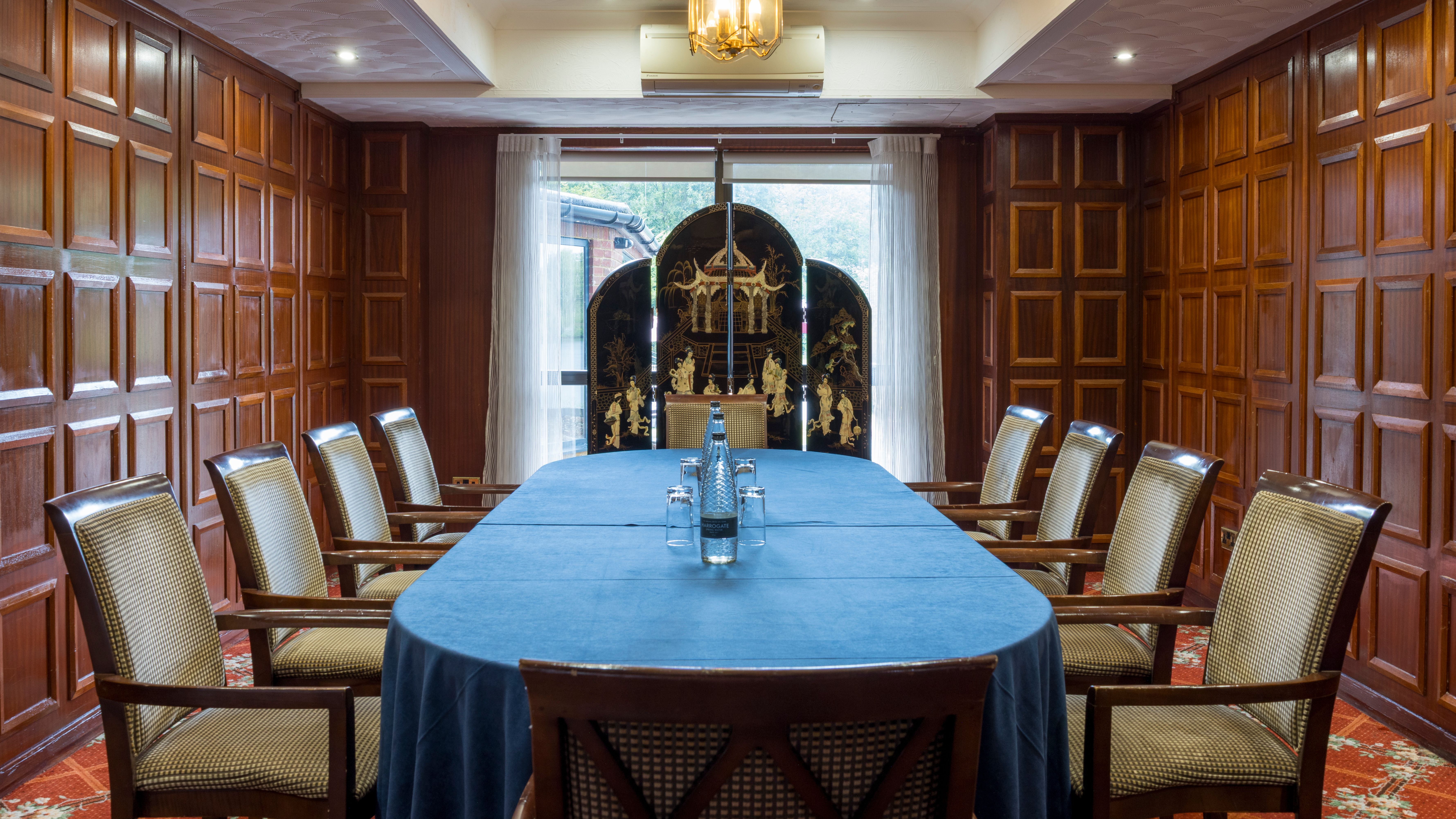 Elegant meeting room with wooden paneled walls, large blue-covered table, and cushioned chairs.