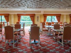 Spacious dining room with red patterned carpet, orange chairs, and large windows with orange curtains overlooking a scenic outdoor view.