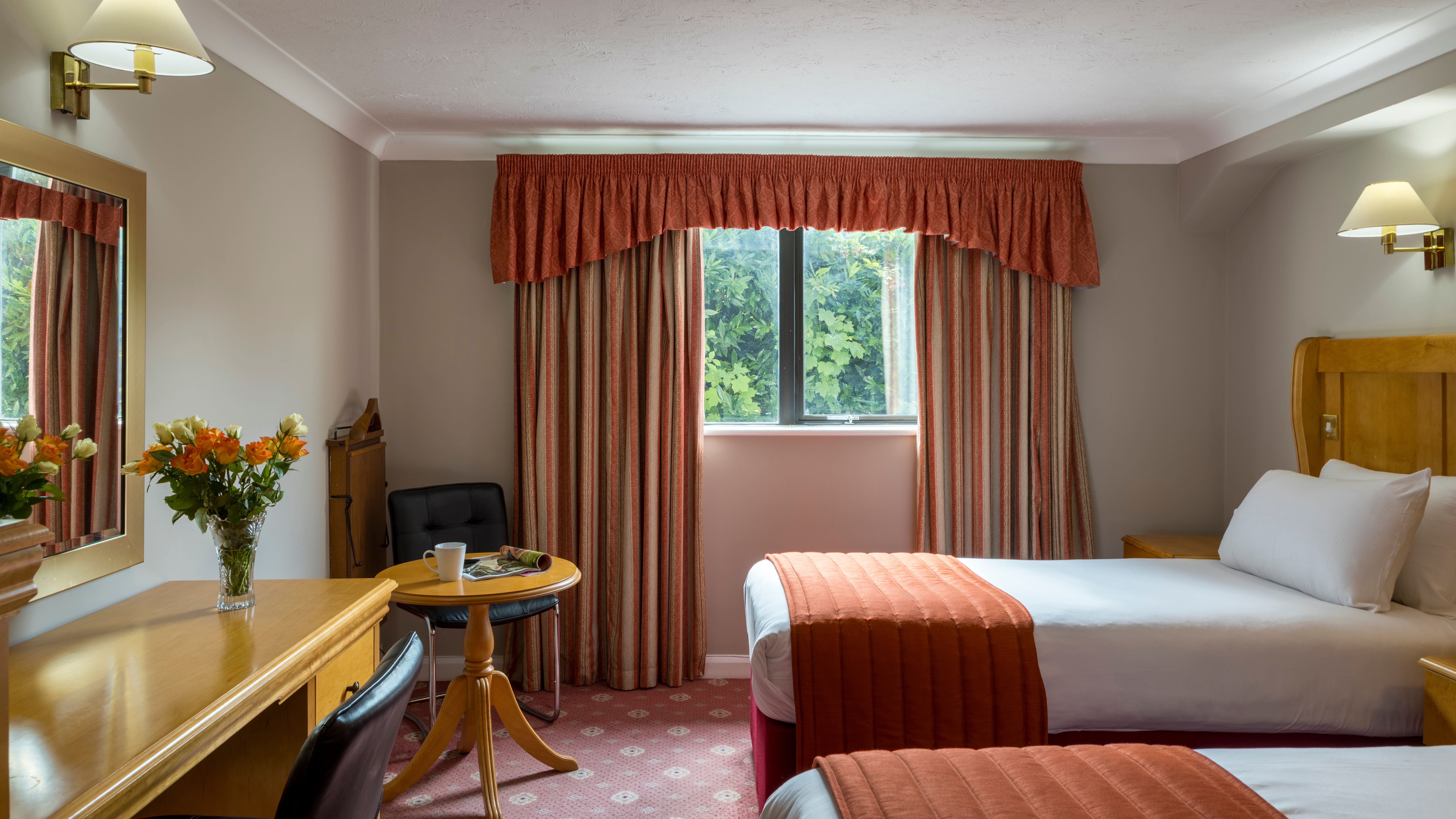 Cozy hotel room with twin beds, wooden furniture, and a window with striped curtains.