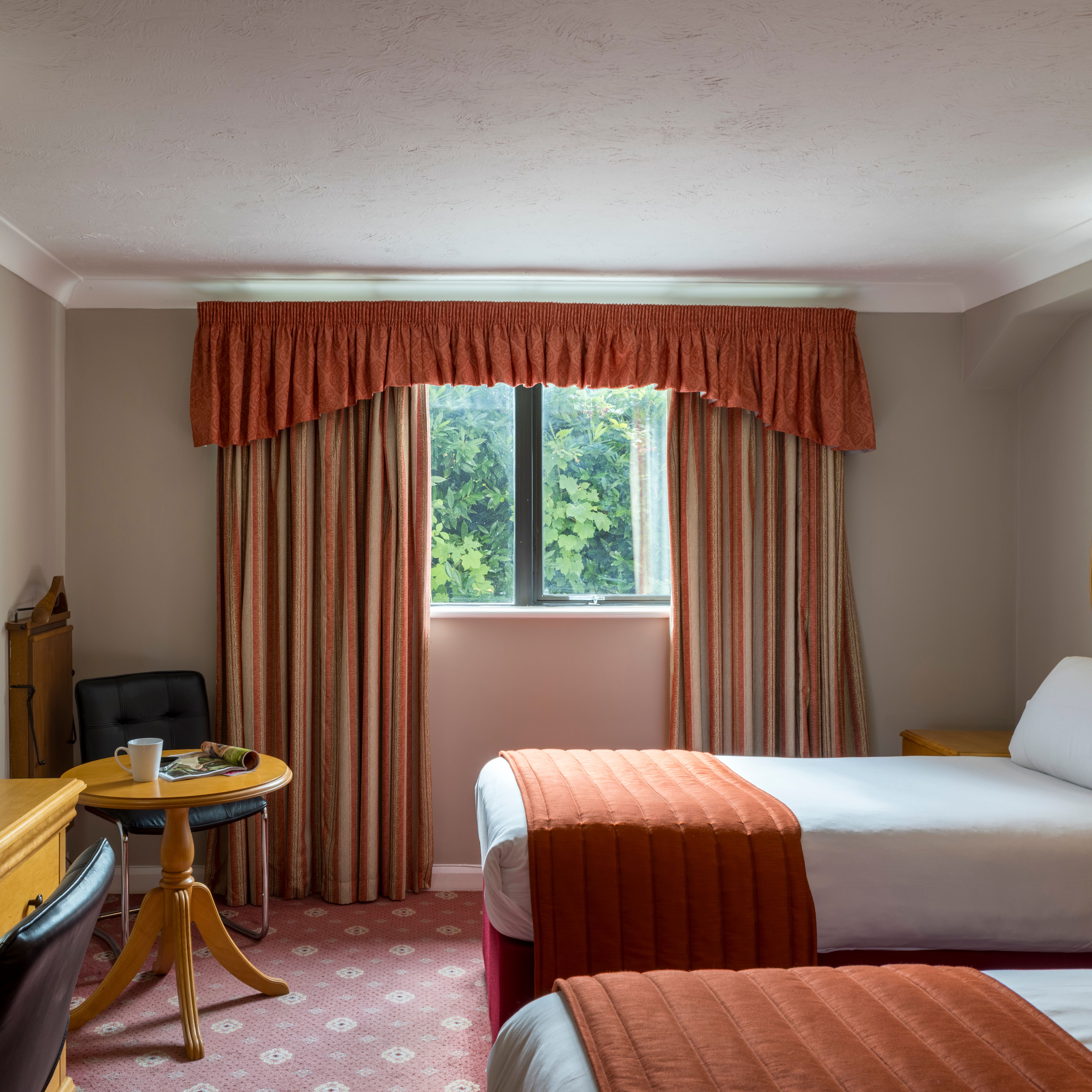 Cozy hotel room with twin beds, wooden furniture, and a window with striped curtains.